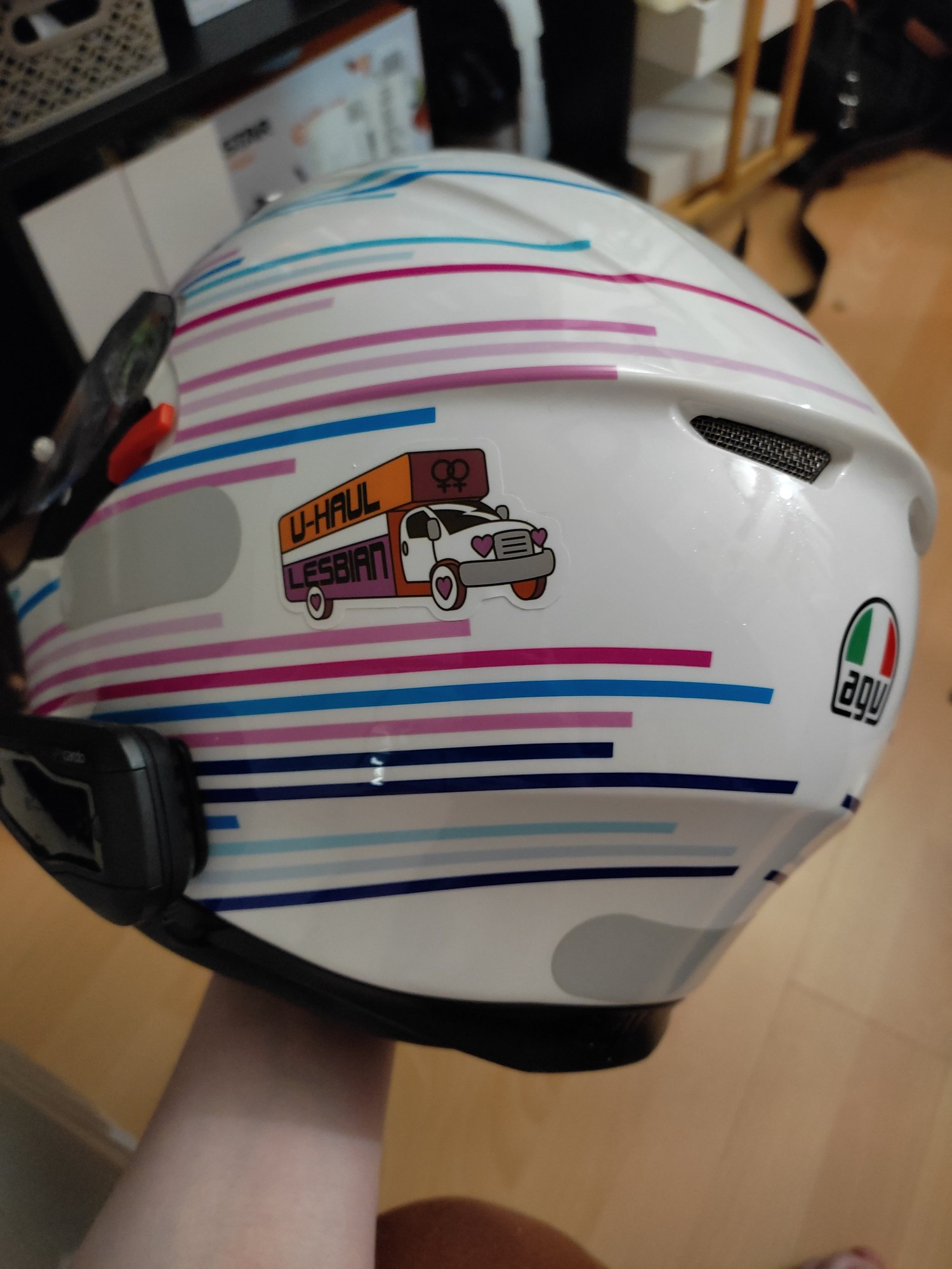 A trans flag colored motorcycle helmet with "U-Haul Lesbian" sticker on it