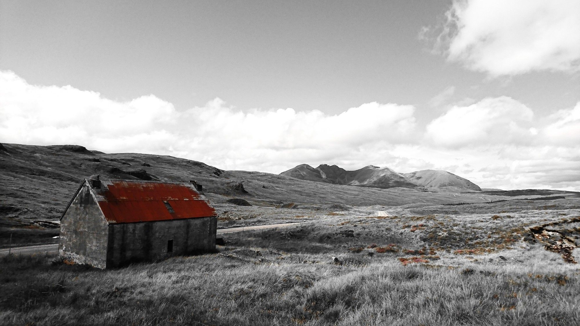 Black and white photo of a moorland landscape with an old bothy alongside a path whose rusty roof is highlighted in colour.