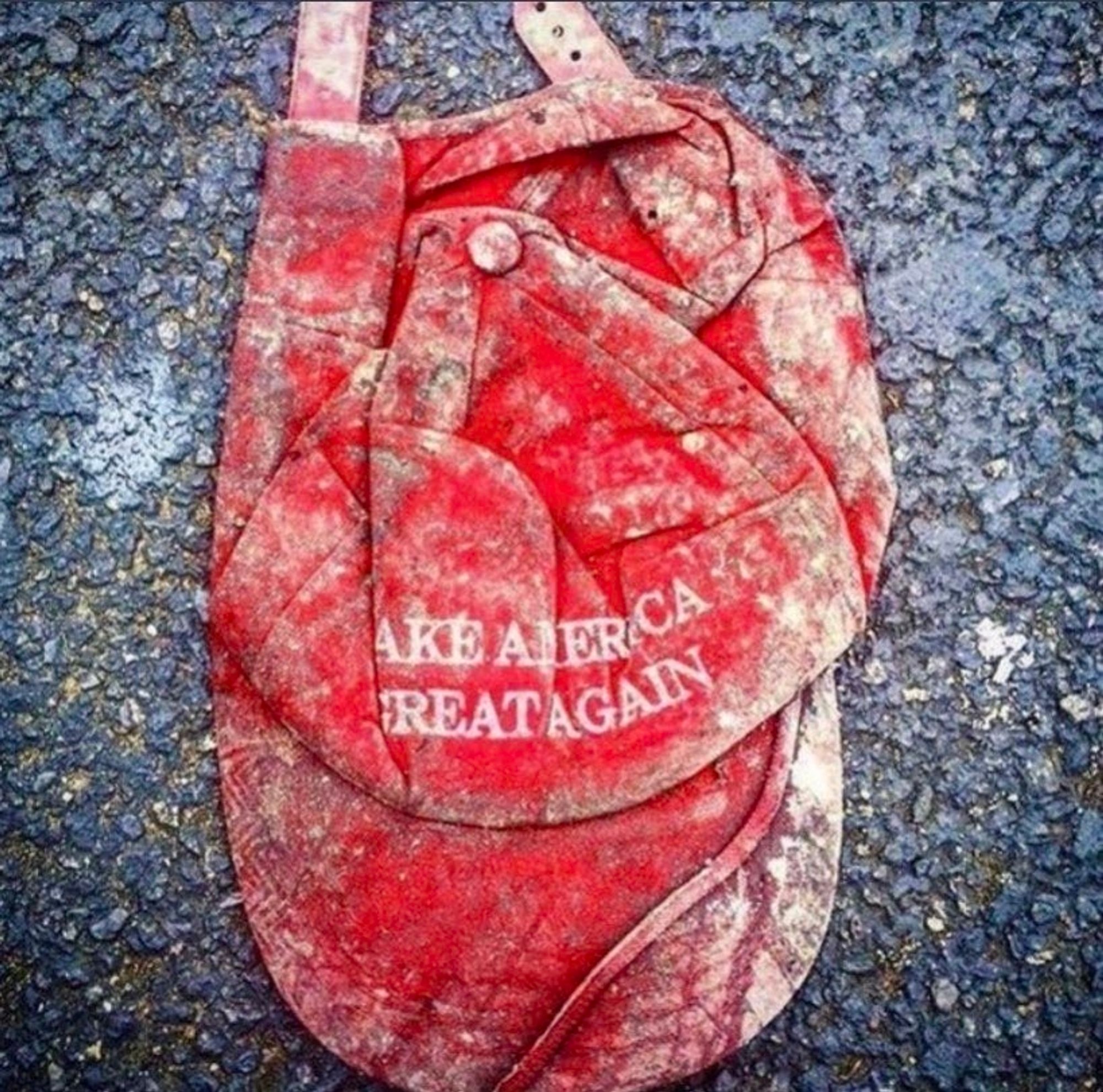 Red MAGA hat left lying on the ground, where it has been trampled.