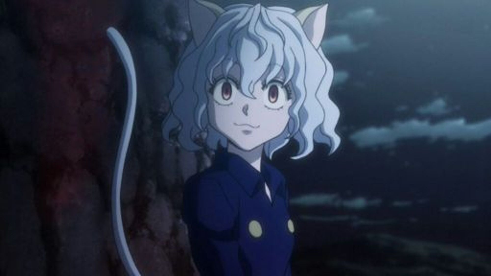 A still of Neferpitou standing at an entranceway of the chimera ant hive, they are a cat person with neck-length wavy white hair and two cream colored cat ears, their eyes are large and piercing and they are wearing a blue jacket.