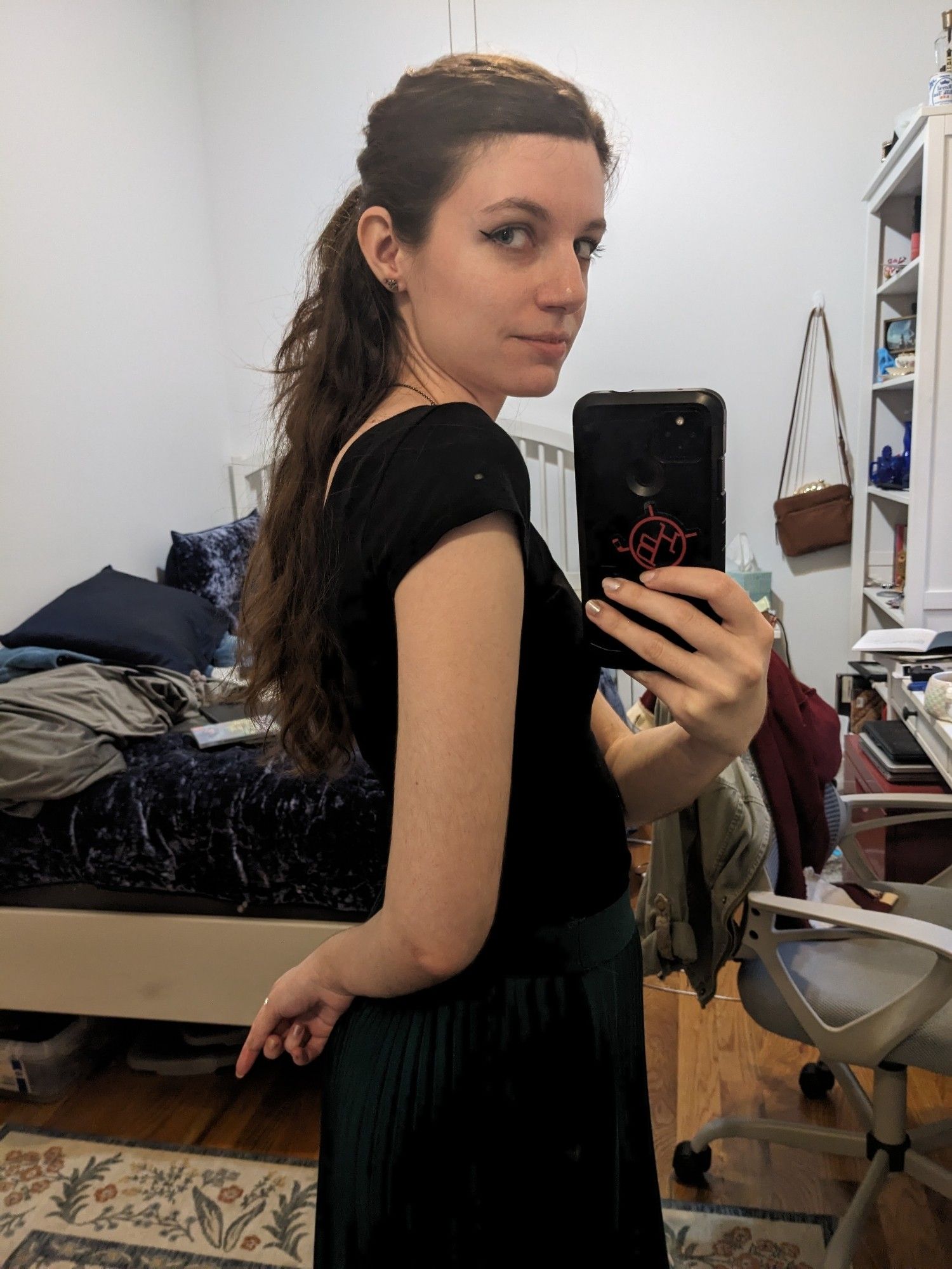 Mirror selfie of brown haired woman in black shirt and green skirt.