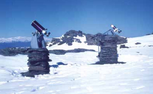 En un paisaje nevado, dos instrumentos parecidos a pequeños telescopios están situados sobre sendas peanas que parecen ser de piedra.