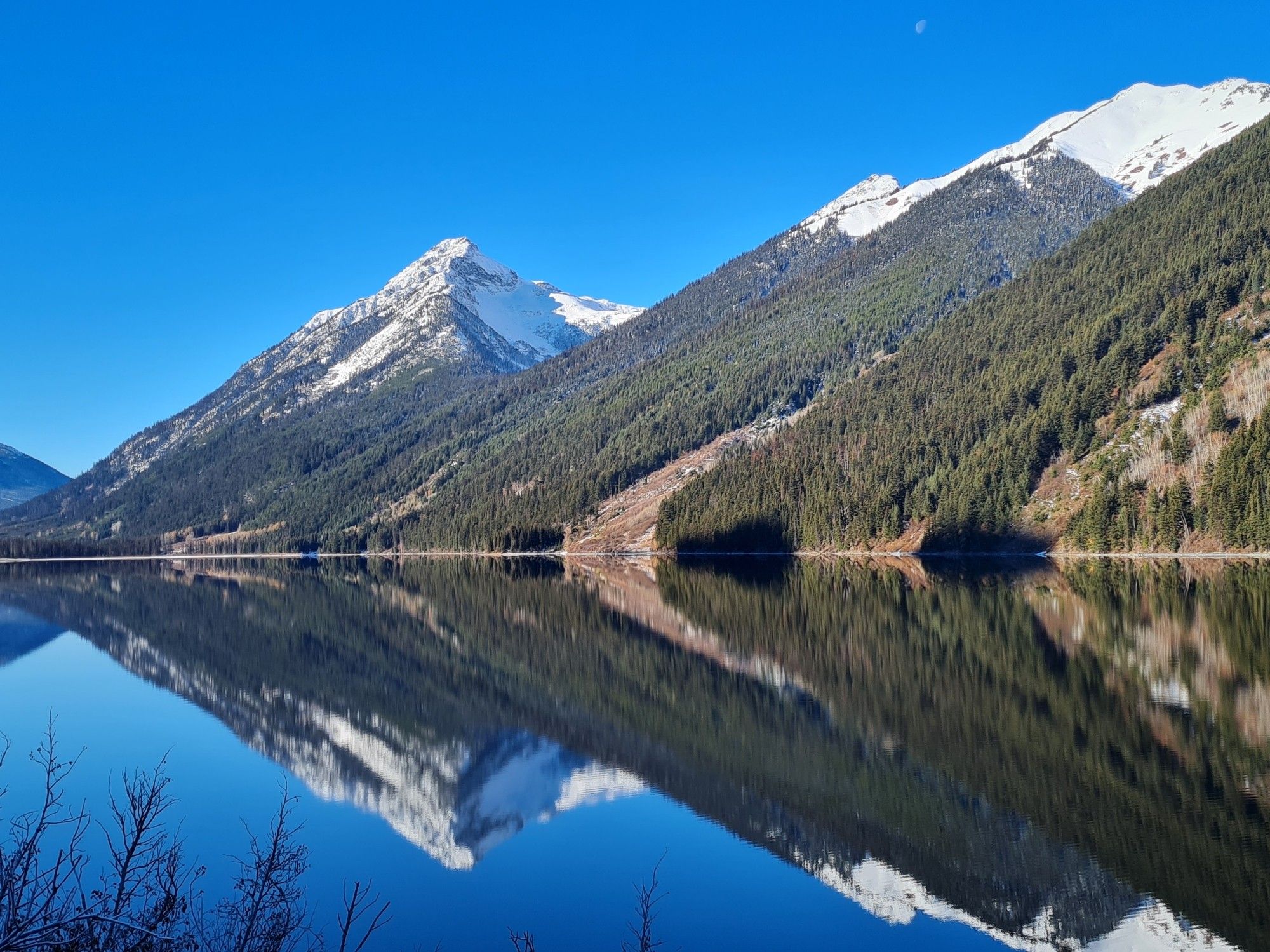 A photo of mountains with snowcaps against a clear blue sky reflected in a mirror like lake