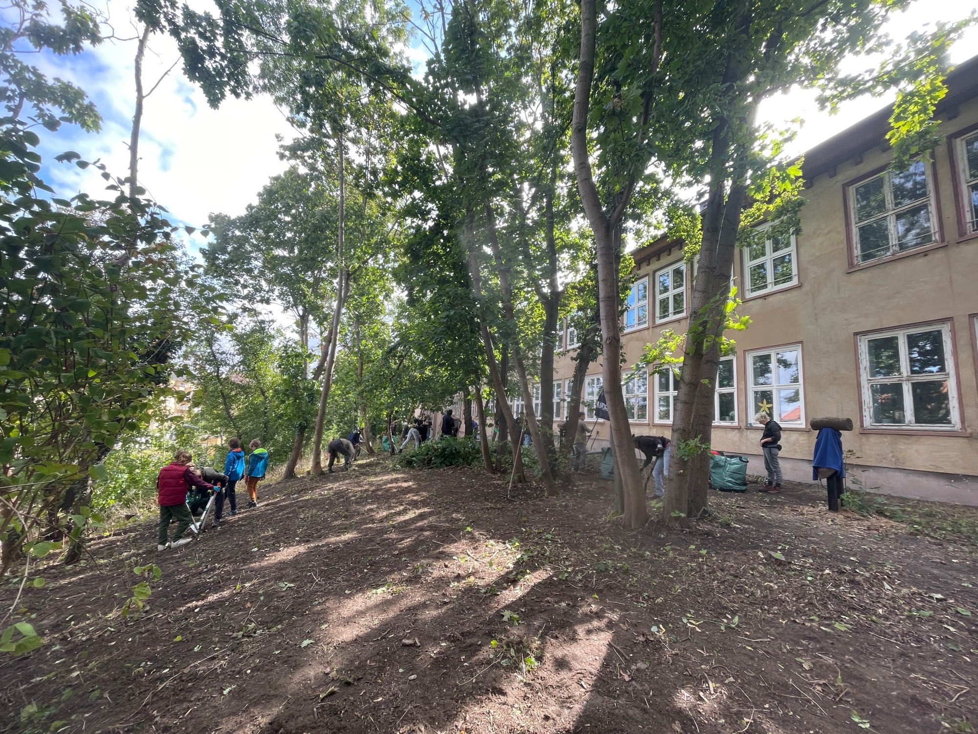 Das Bild zeigt zahlreiche Menschen, die auf der Gartenfläche vor dem Haus im Einsatz sind – vor ihnen liegt eine bereits große von Wildwuchs befreite Fläche.