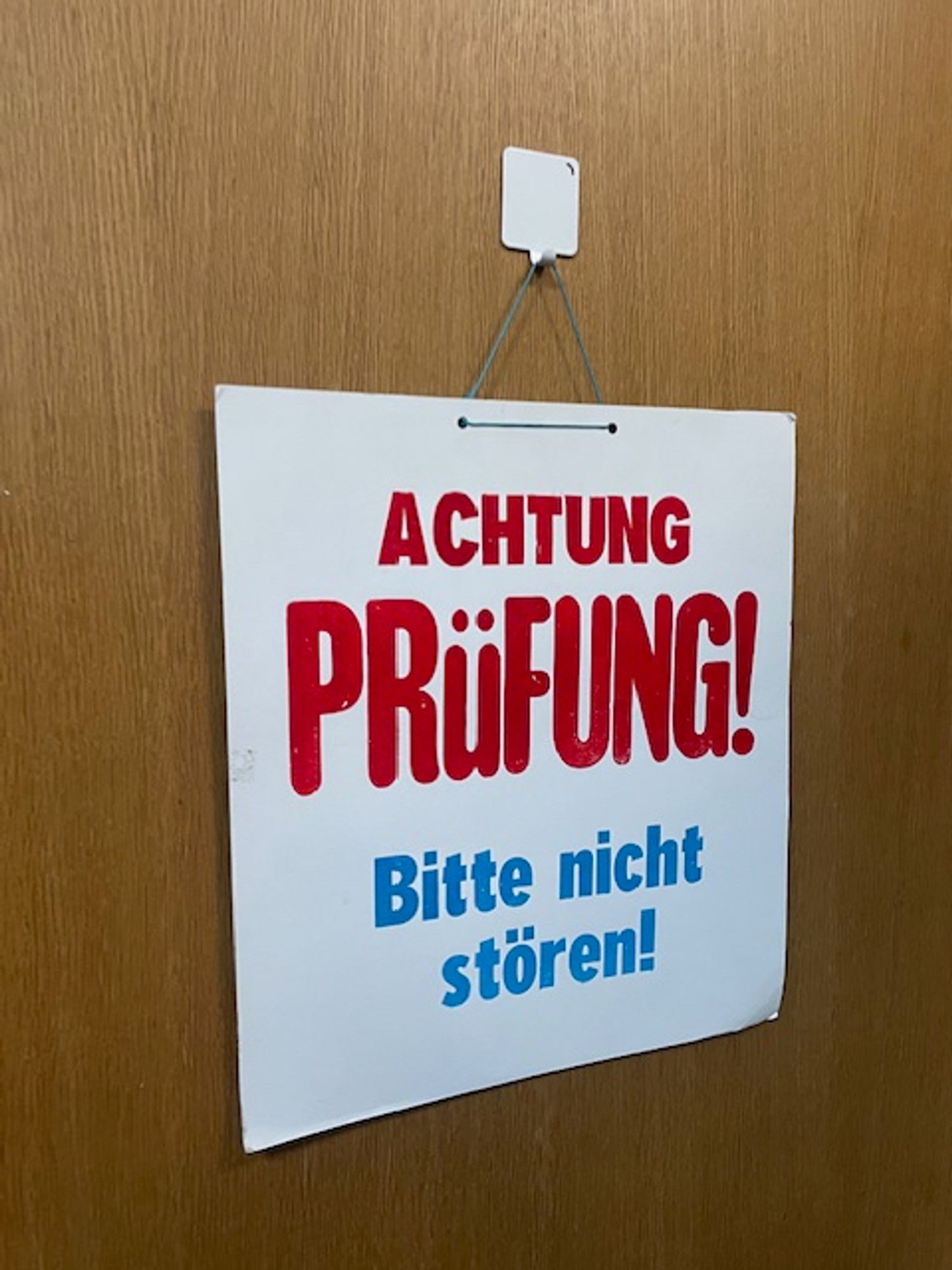 Das Bild zeigt ein gedrucktes Schild an einer Tür, auf dem in rot und blau „Achtung Prüfung! Bitte nicht stören!“ steht.