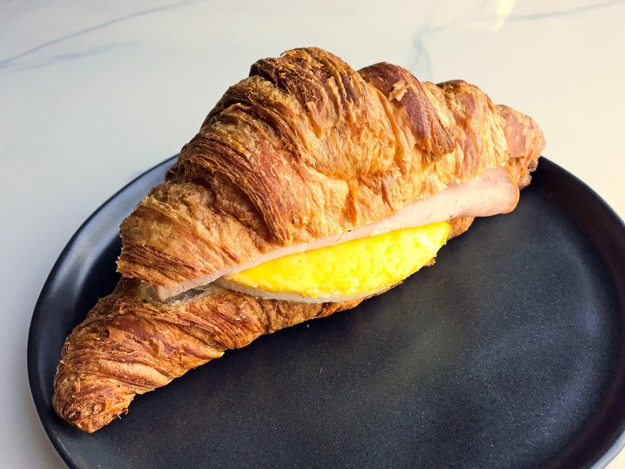 A croissant sandwich with fried egg and ham peeping out.