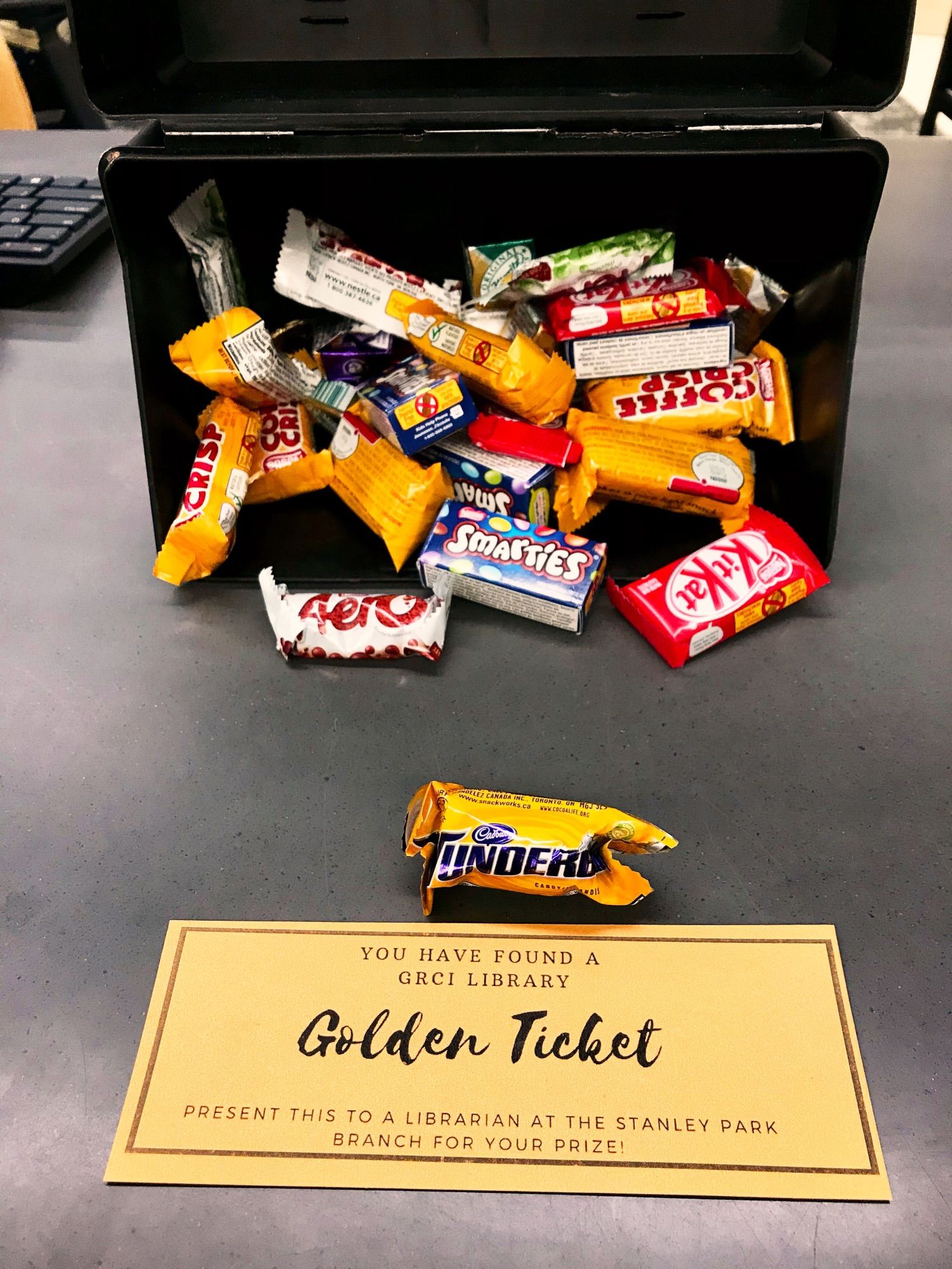 A mini Wunderbar sits in front of my golden ticket. In the background is a box filled with other mini chocolate bars - KitKat, Smarties, Aero, Coffee Crisp.