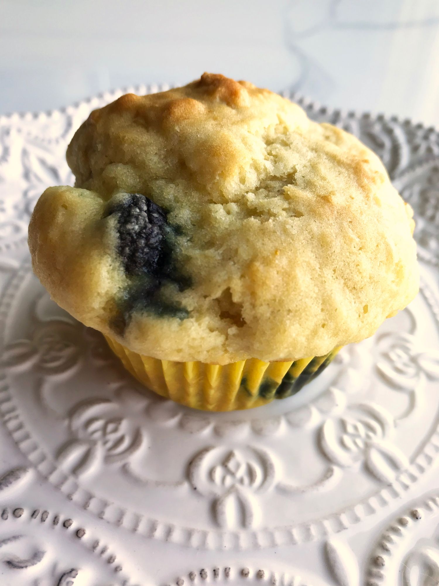 A dappled, blueberry-smudged, puffy-topped muffin on a semi-fancy quarter plate.