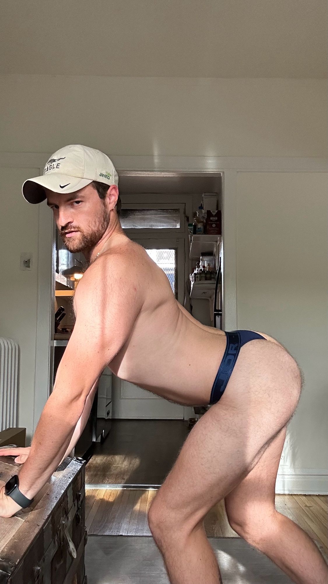 Thirst trap of me from the side, leaning forward on a trunk so I’m on all fours, wearing nothing but a skimpy blue thong and baseball cap