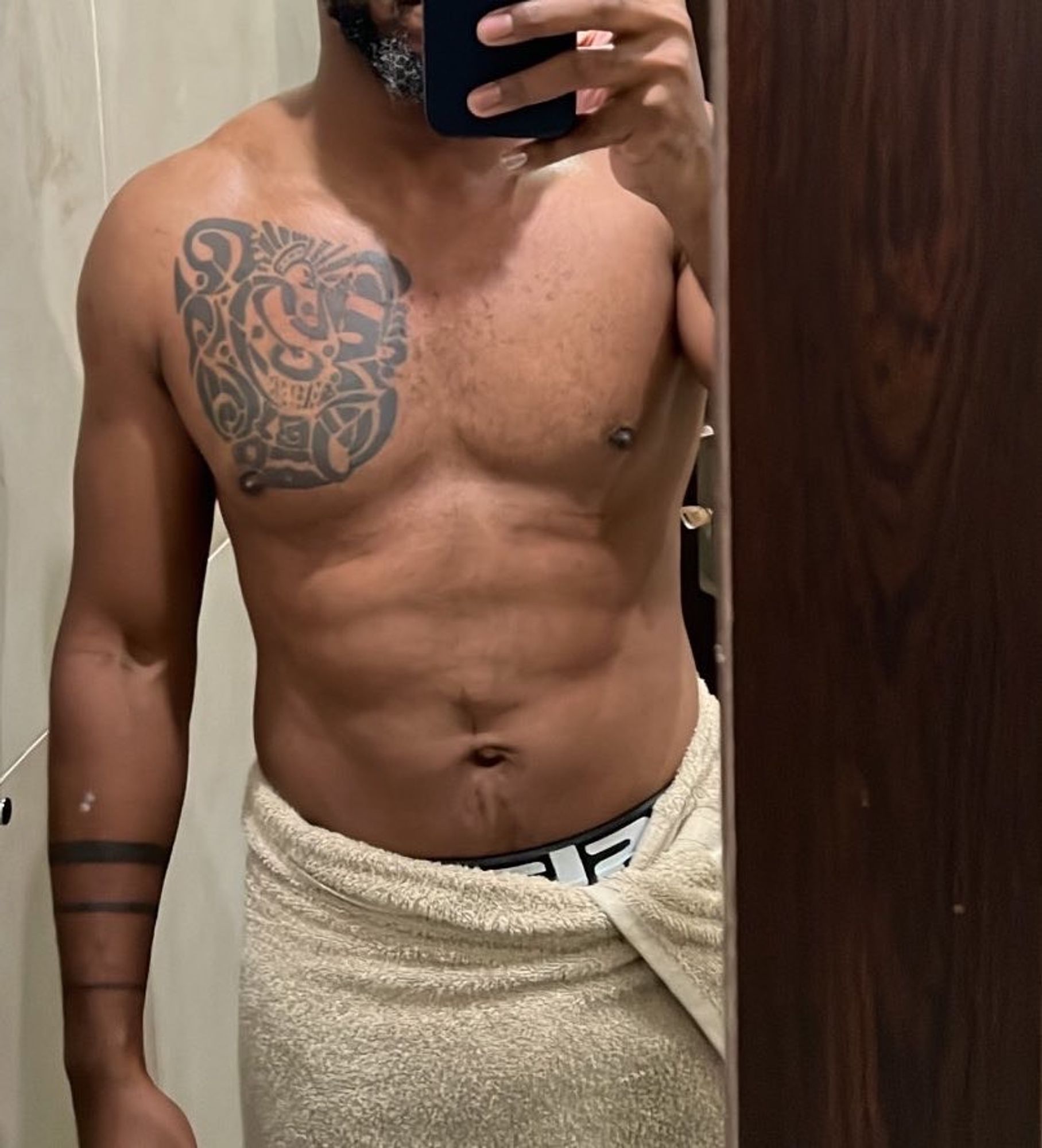 A bare chested black man mirror selfie. He has a unique pectoral tattoo stage left and three tattooed strips on his arm stage left. 
He’s wearing a towel with underwear peeking 

On a scale of 1-10 he’s a 7 in fitness and muscle definition