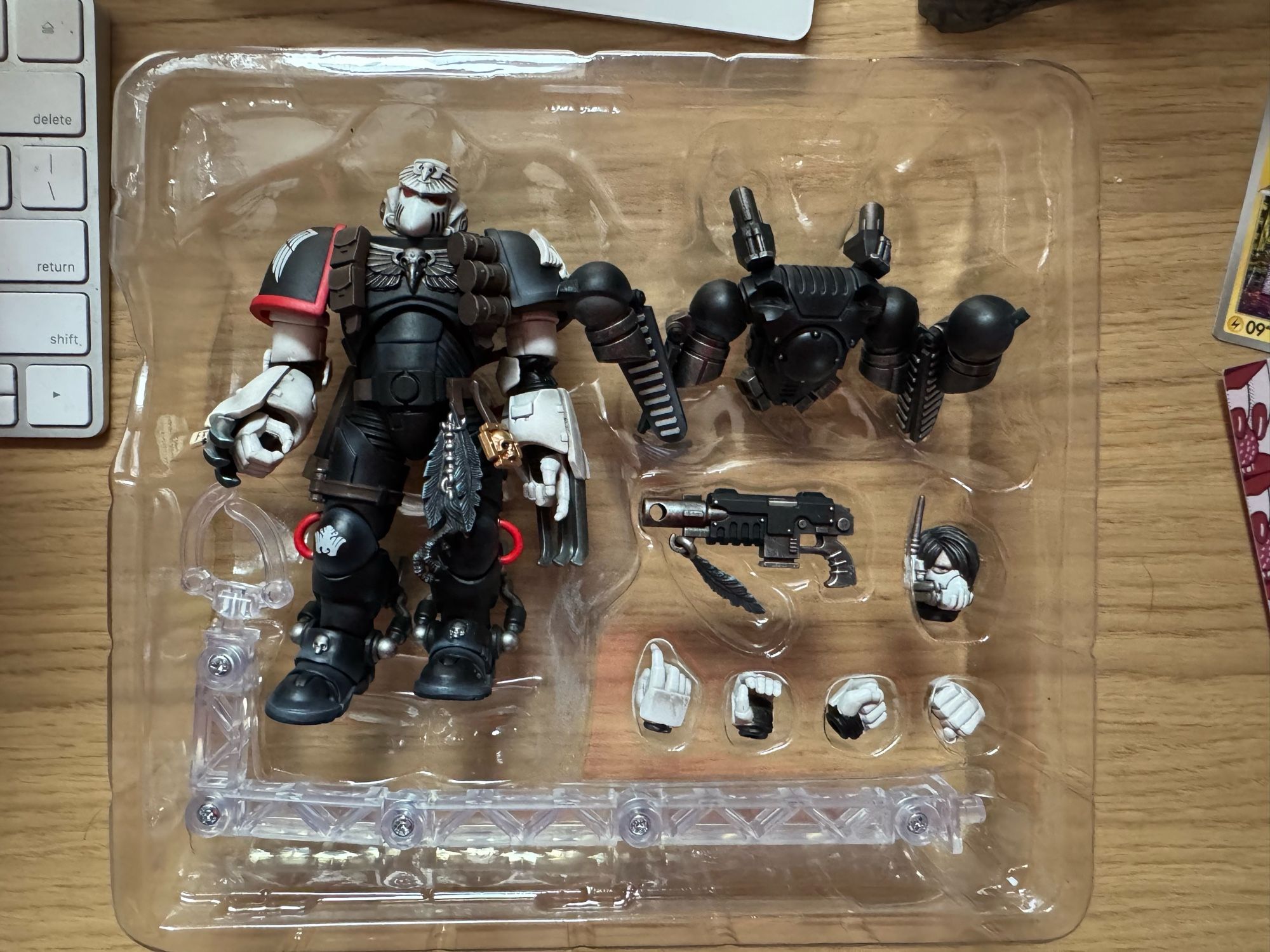 A boxed figure of joytoy Raven Guard chapter master Shrike; the right knee deck is upside down and two parts of the backpack are visibly broken off