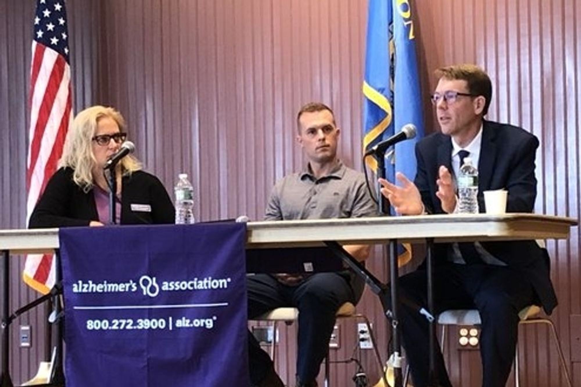 Two people with important jobs stare at a third person who is talking into a microphone and doing something or other with his hands.