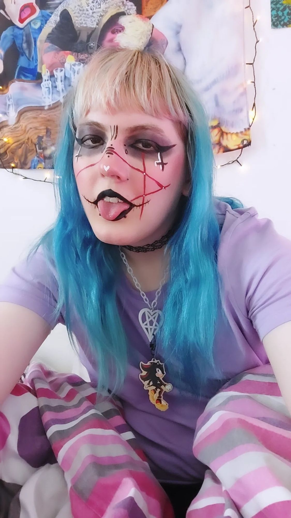 a very strange looking thing in bed with blue and pinkish hair with gothic makeup and runes on her face. her tongue is out and she's wearing a necklace with a heart shaped pentagram and shadow the hedgehog.