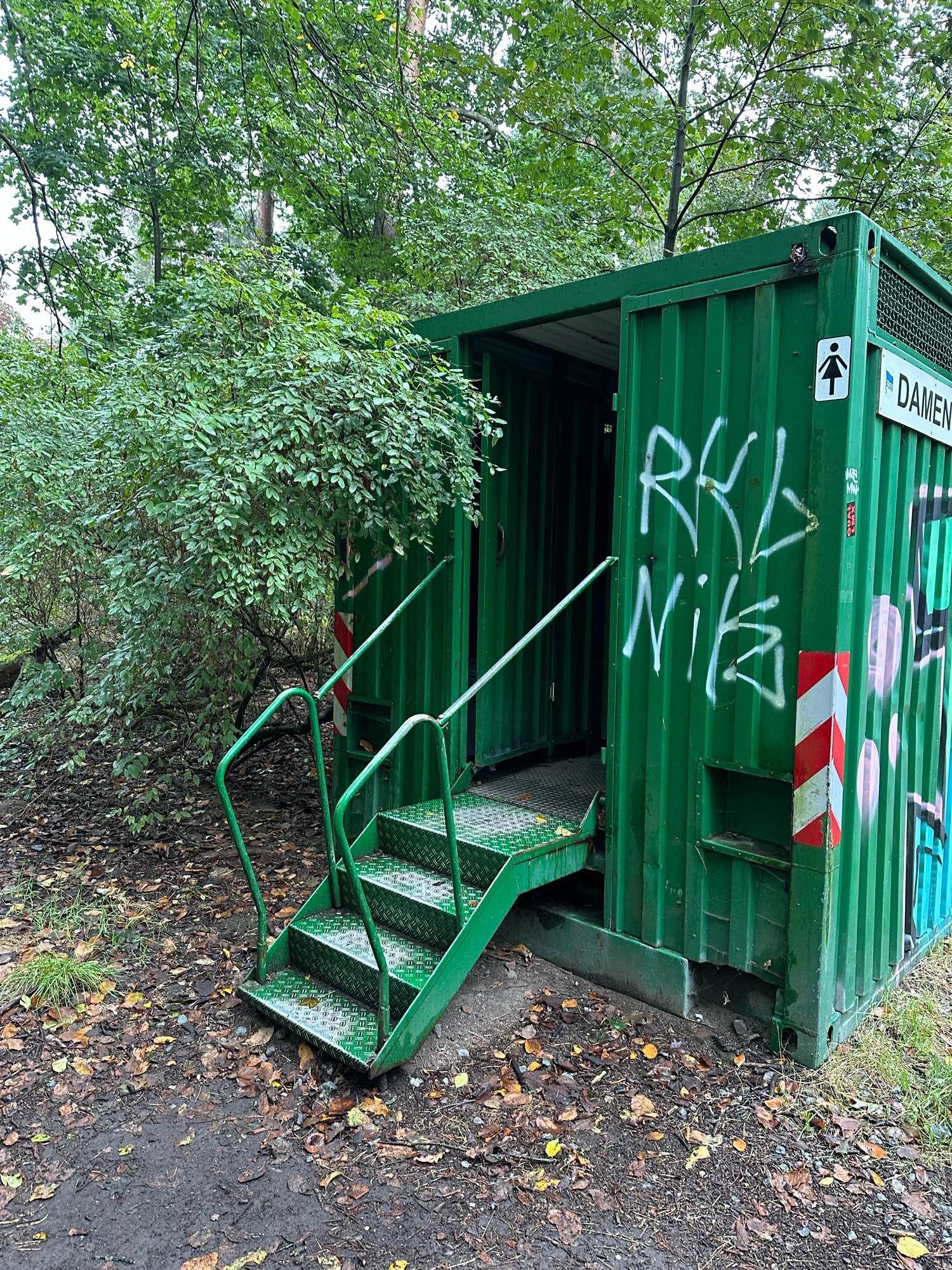 Grüner Toilettencontainer mit Treppe im Wald.