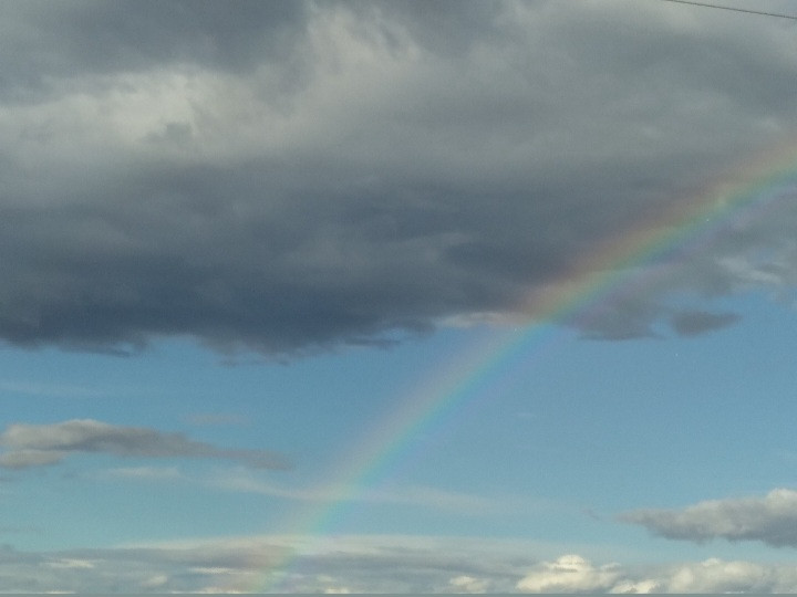 Image of grey clouds and rainbow over a blue sky