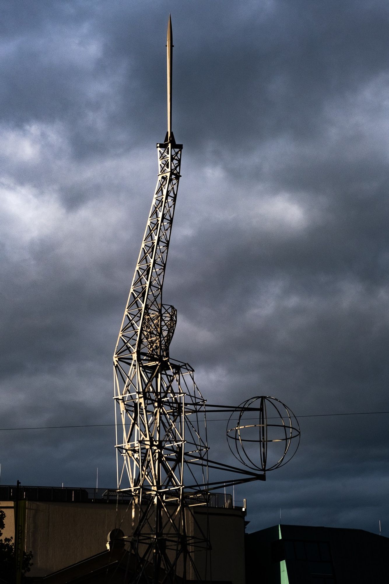 Eine aus Metallstreben der New Yorker Freiheitsstatue nachempfundene Statue. Sie wird von der linken Seite von der Morgensonne beschienen. Im Hintergrund sind ganz dunkle Regenwolken.