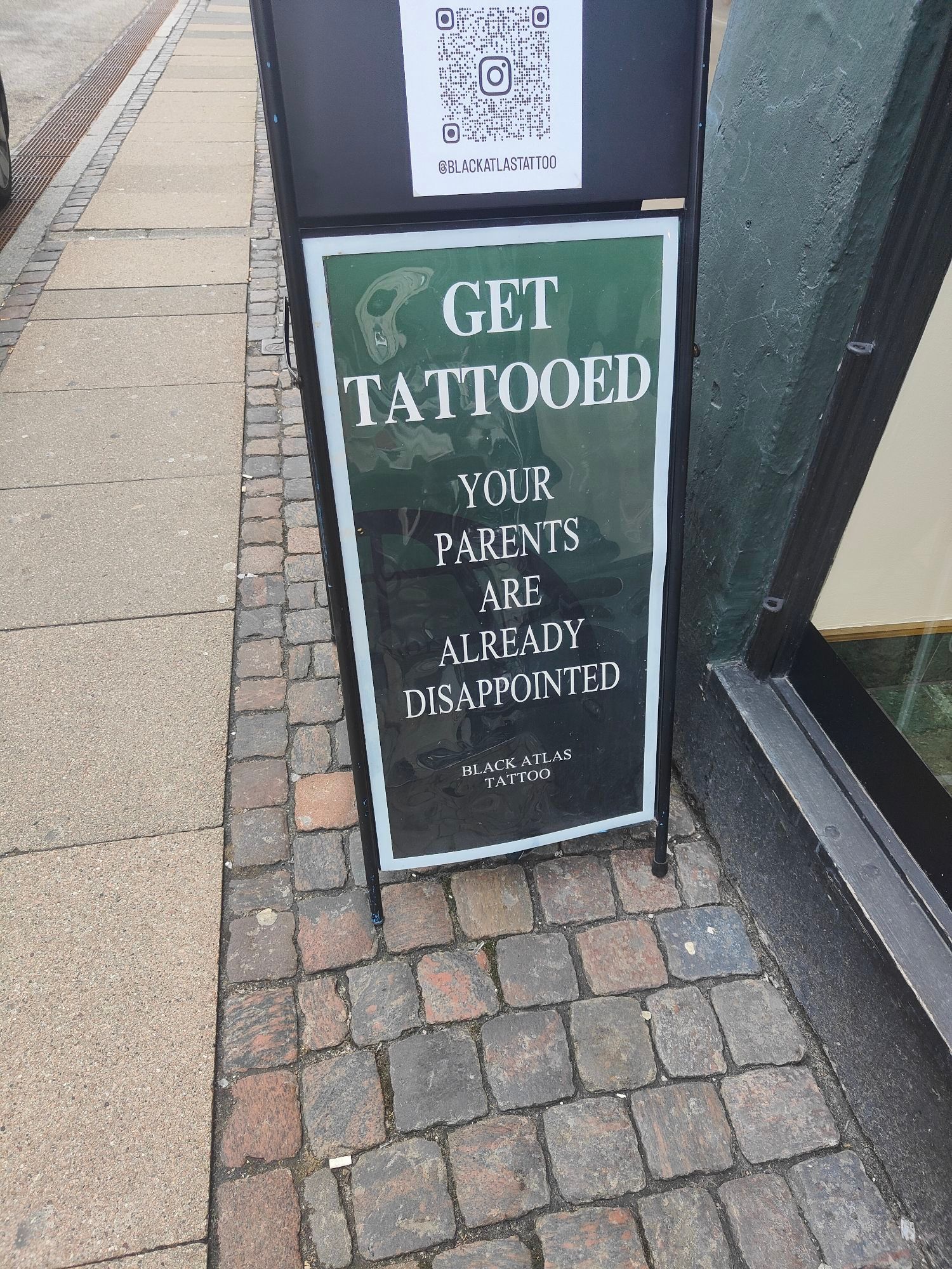 Sandwich board sign reading "Get tattooed - your parents are already disappointed"