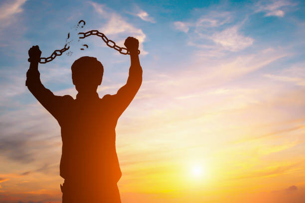 man in silhouette breaking the shackles on his arms in front of a beautiful sunset