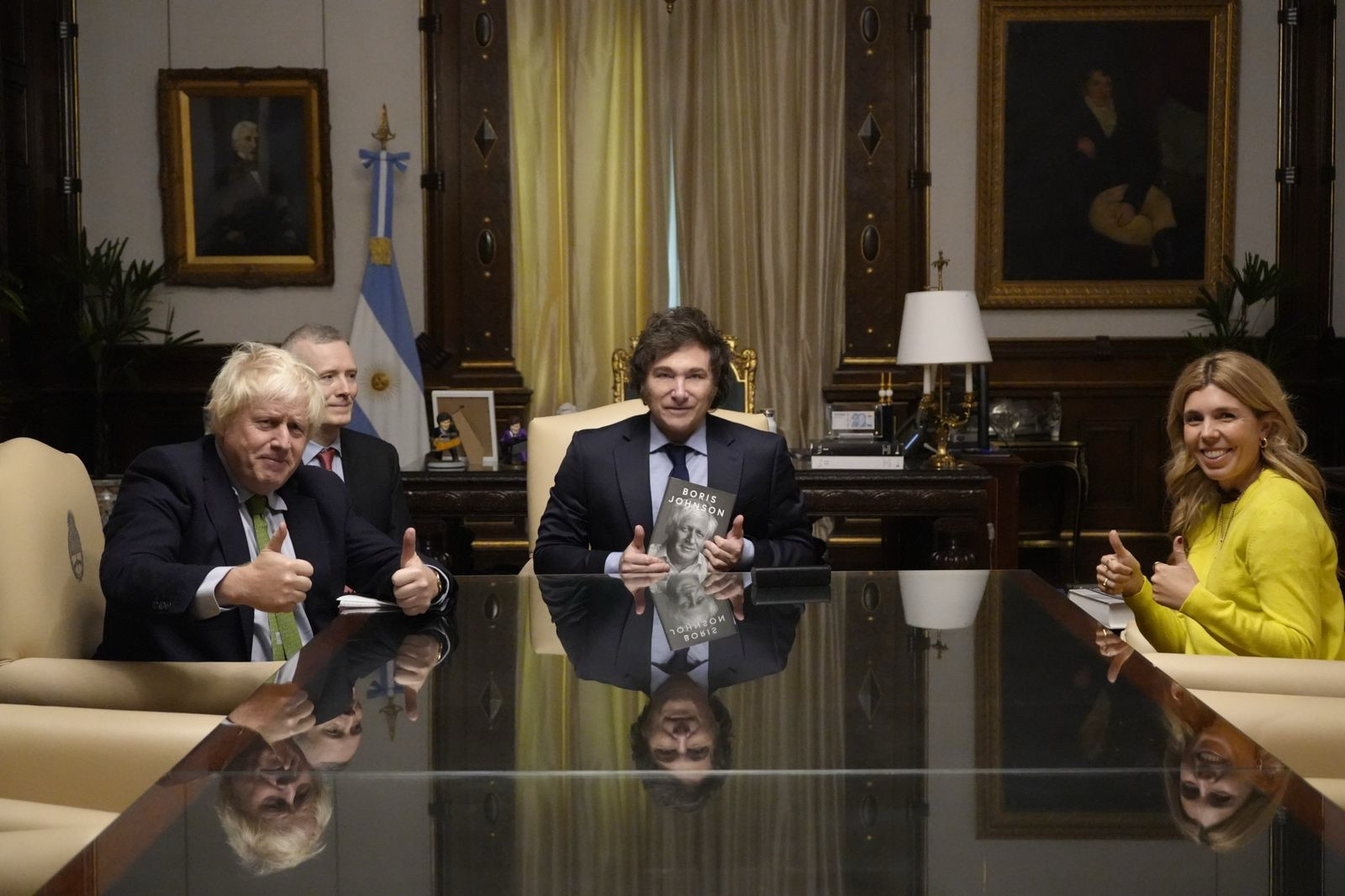 Johnson, Milei and woman in yellow do thumbs up at a big table 