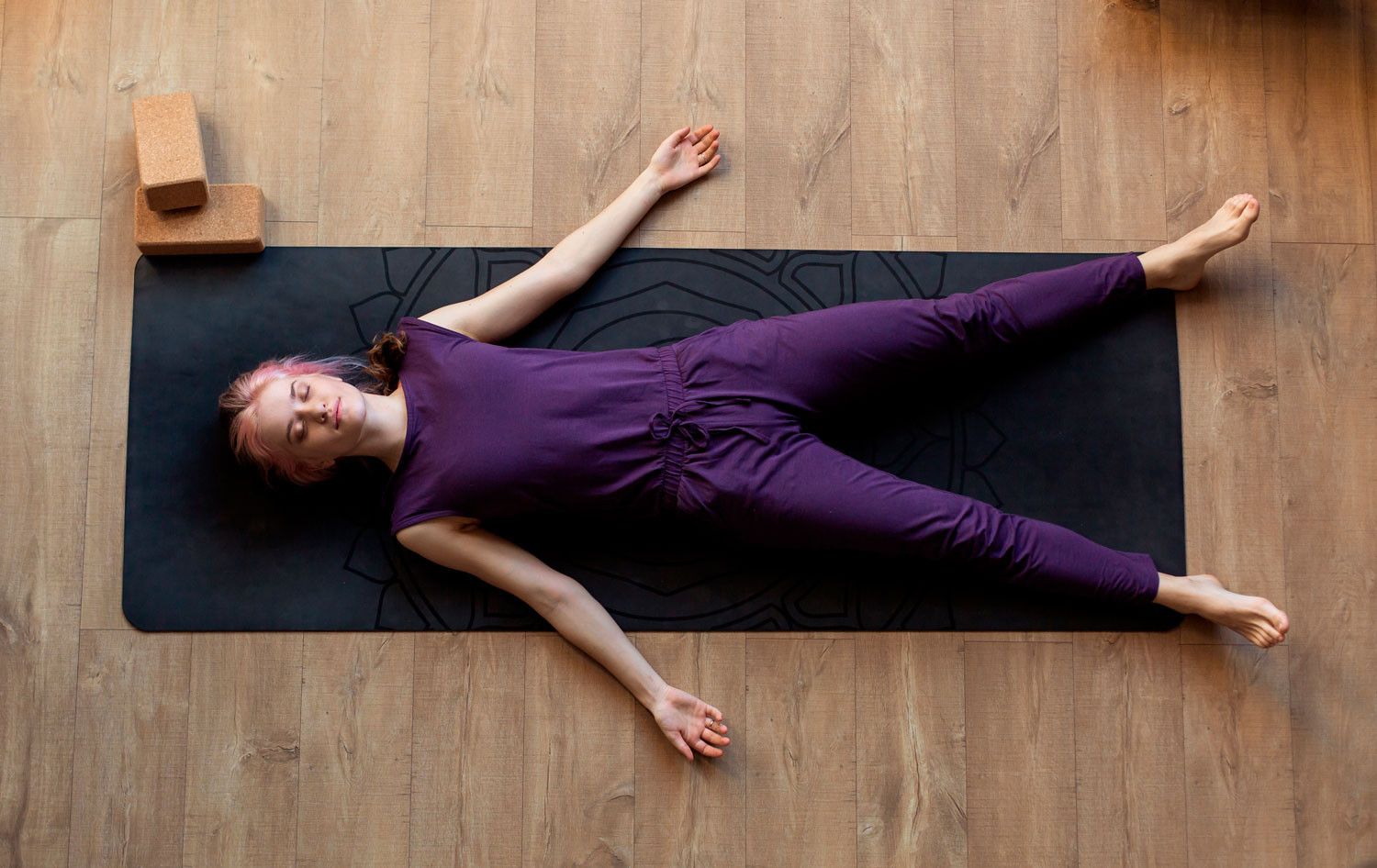 A woman in Shavasana (corpse pose). She is lying on a yoga mat.