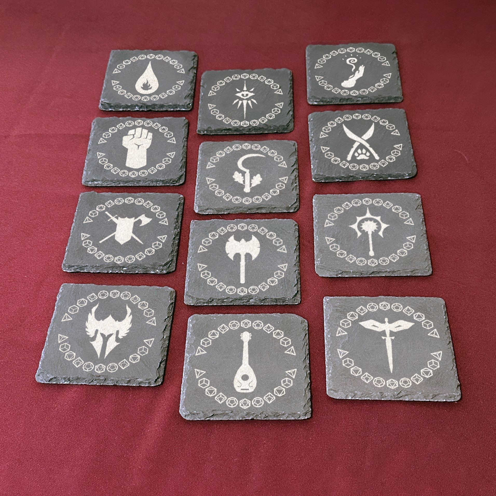 Twelve slate coasters in 3 columns and 4 rows. Each coaster is engraved with a different dungeons and dragons class design, surrounded by various types of dice.