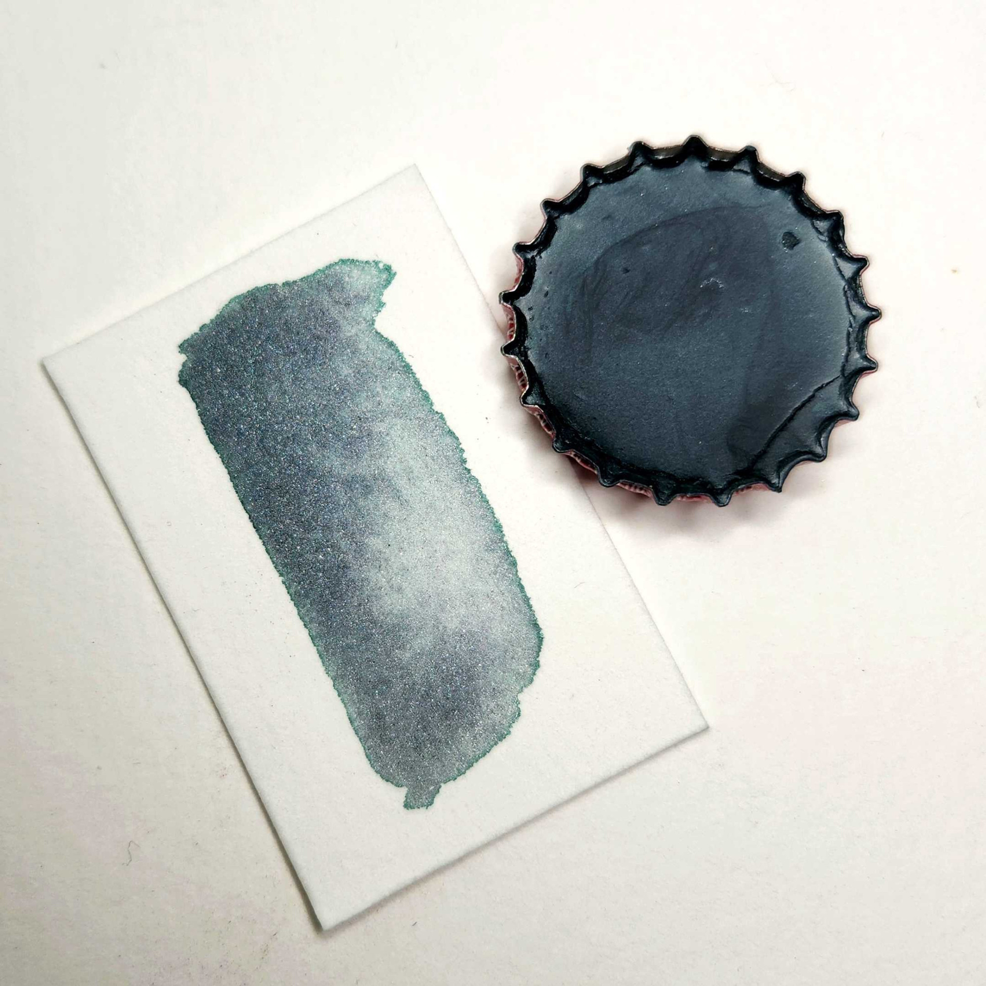 photo of a paint stored in a bottle cap. the color is a neutral phthalo green-gray with silver mica sparkles.