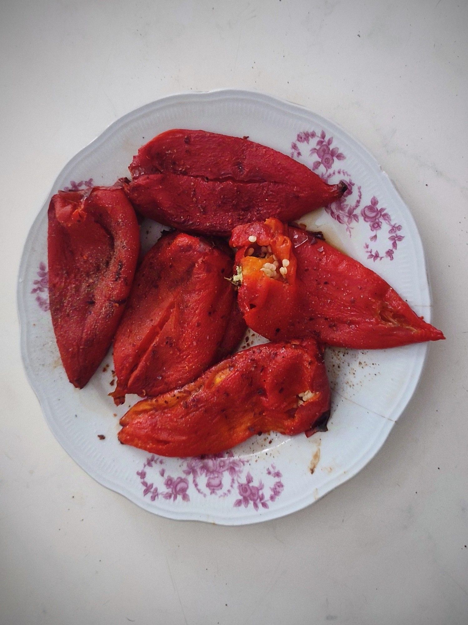 Five roasted and peeled capia pepper on a large plate.