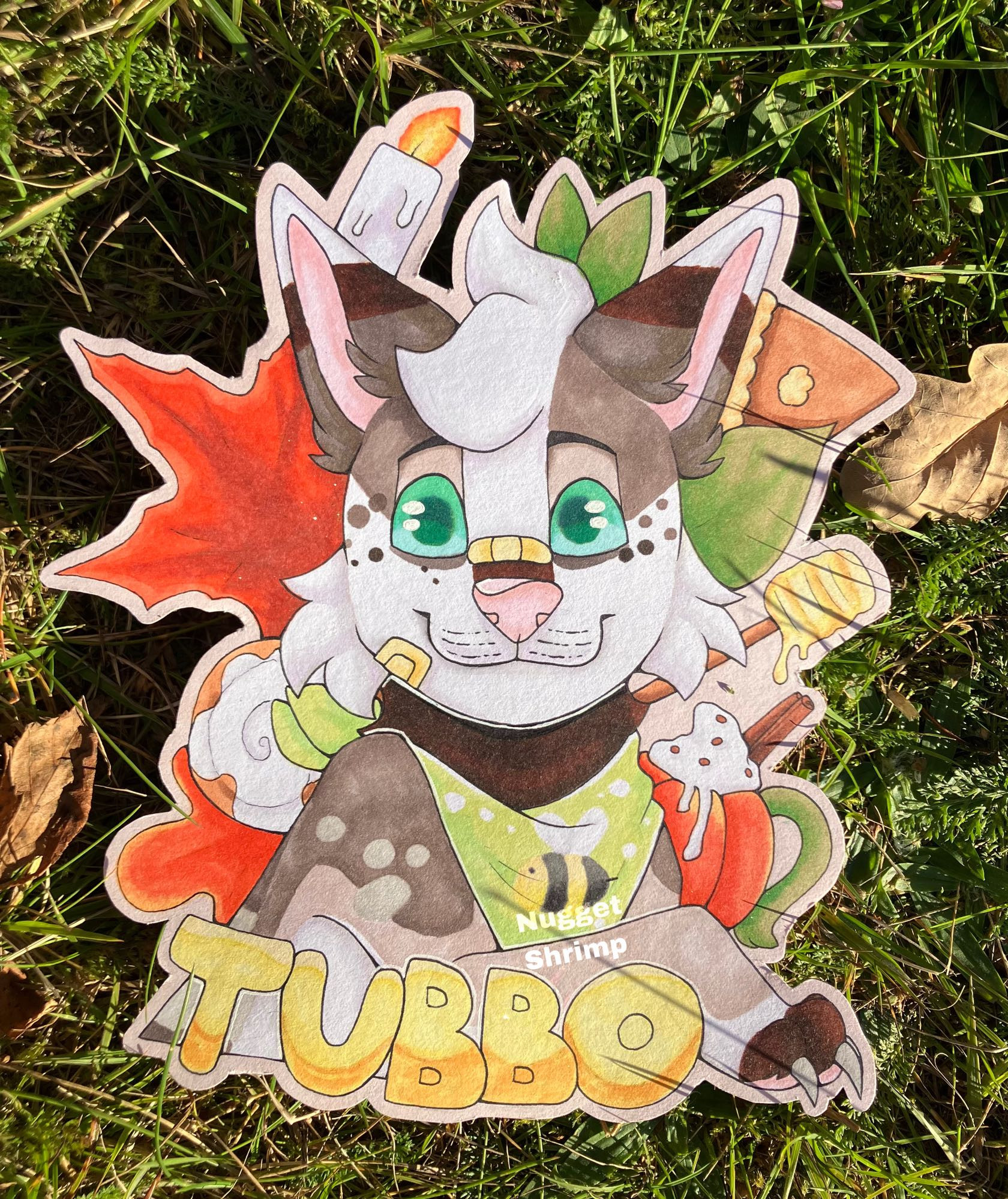 Front facing cartoony fox. Leaves, a drink and other autumn objects are behind him.  Lower down there's big yellow text saying "Tubbo" as it's his name. 