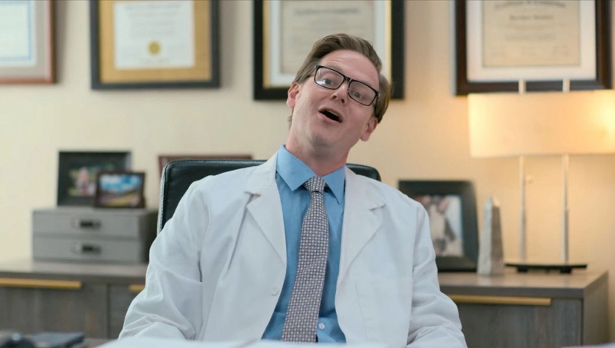 Tim Heidecker as a doctor in the ABX Heart Monitor sketch from ITYSL. He’s sitting at an office desk, leaning back and speaking. There is no caption.