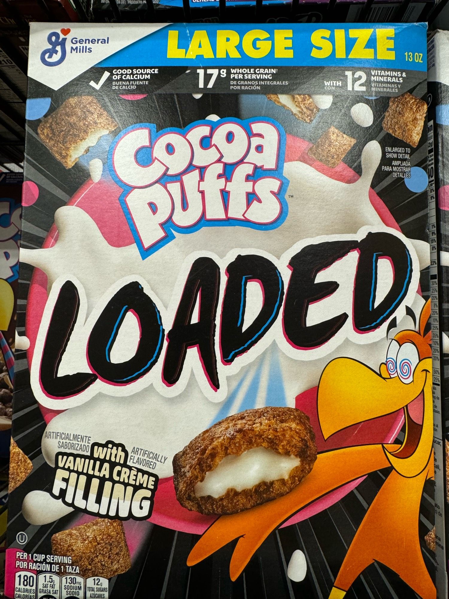 A cereal box for Cocoa Puffs Loaded with vanilla crème filling showing a burst of white goo and the bird mascot looking at a cereal with hypno eyes