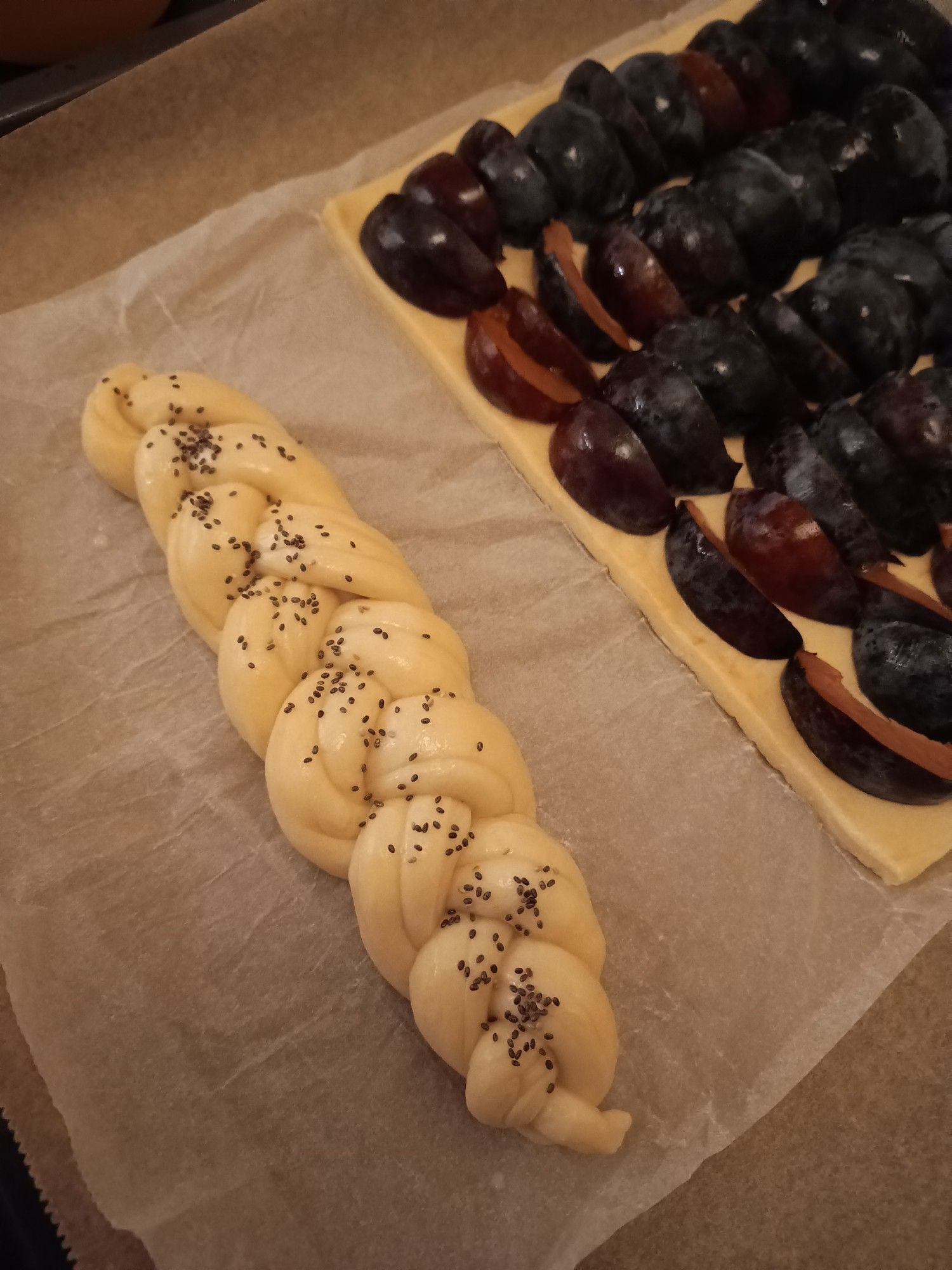 Uncooked braided challah topped with black seeds sitting on baking paper next to an uncooked plum tarte