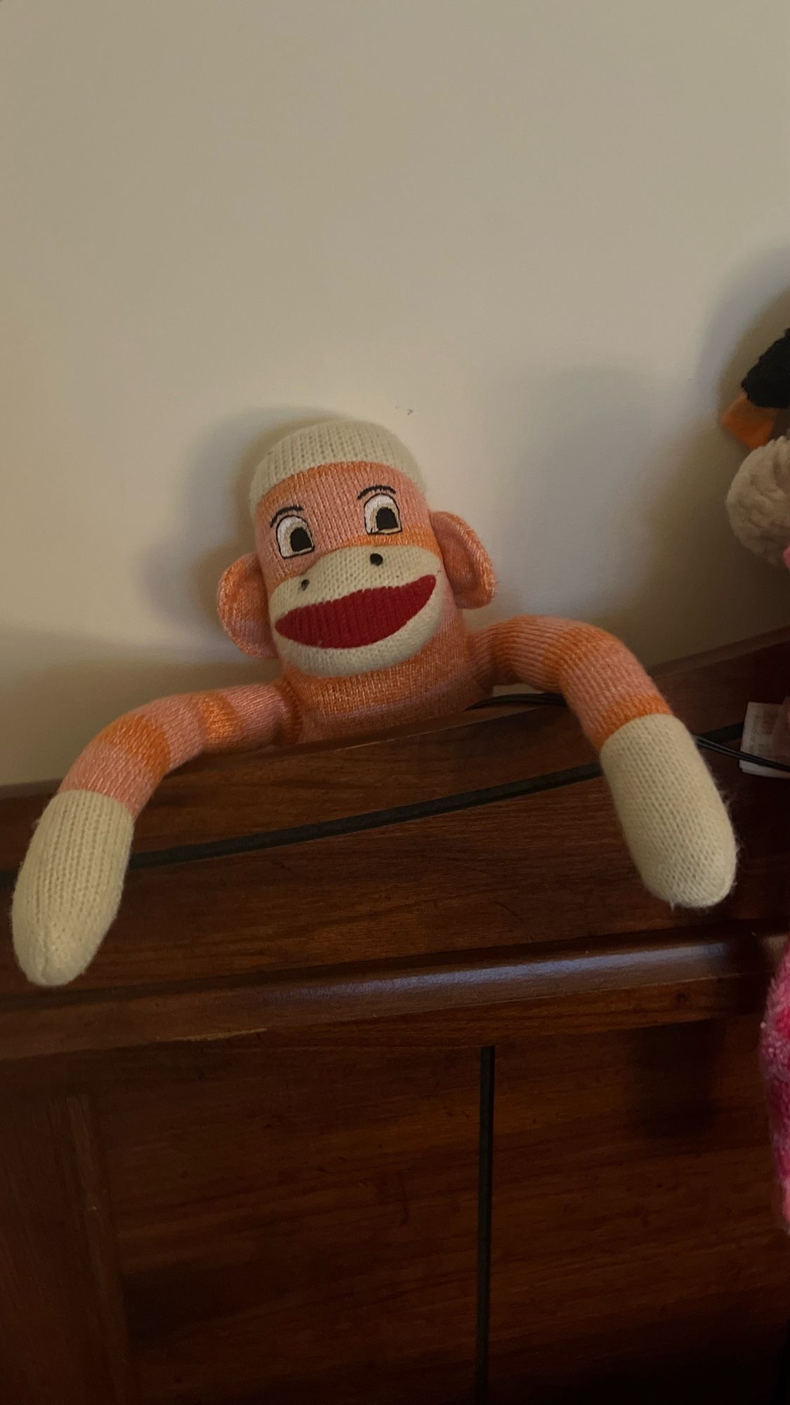 A skeptical sttffed sock monkey emerging from behind a headboard of a bed