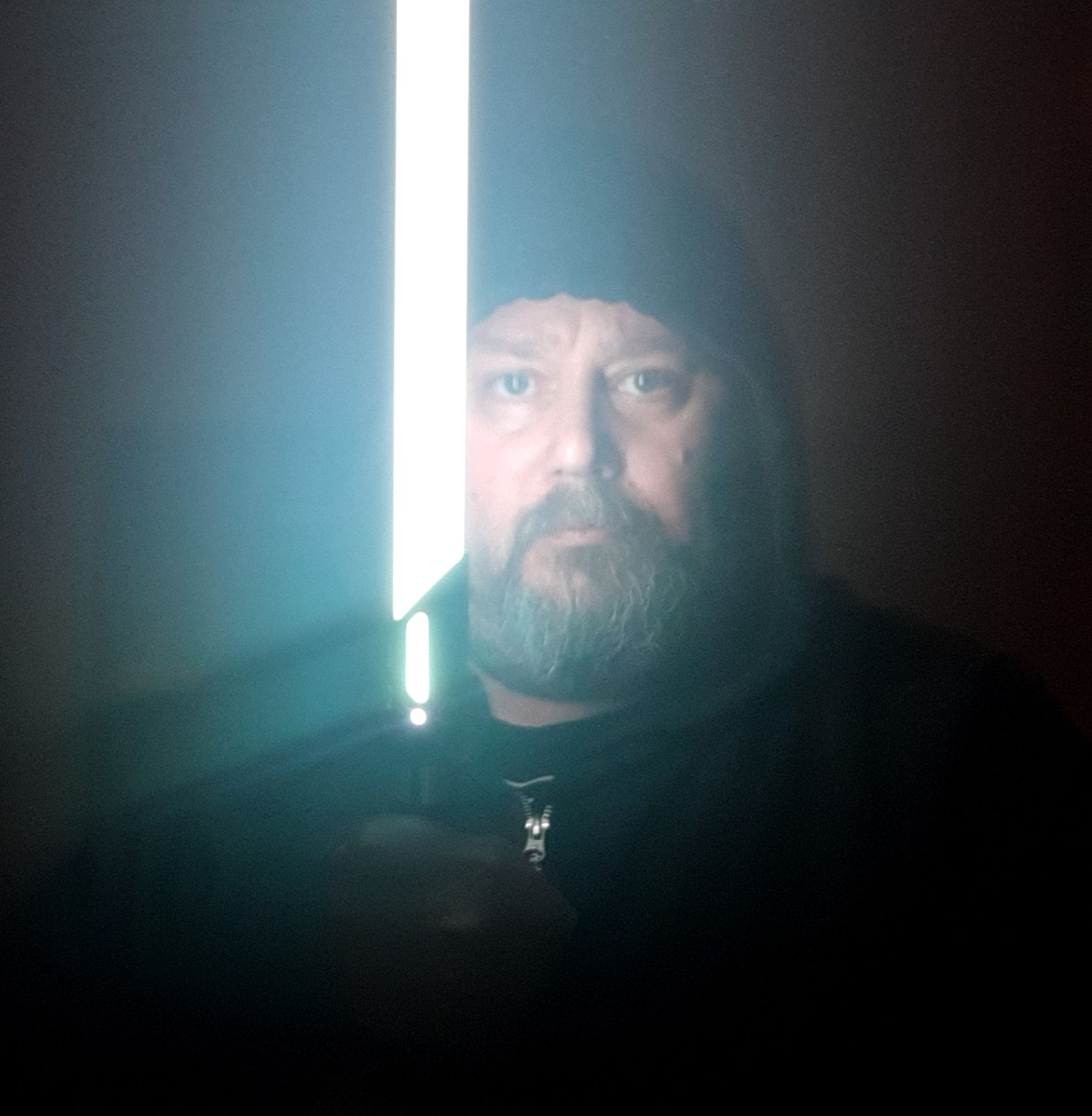 Photo of Cody Menzies, dressed in a hoodie and holding a lightsaber. He looks goofy.