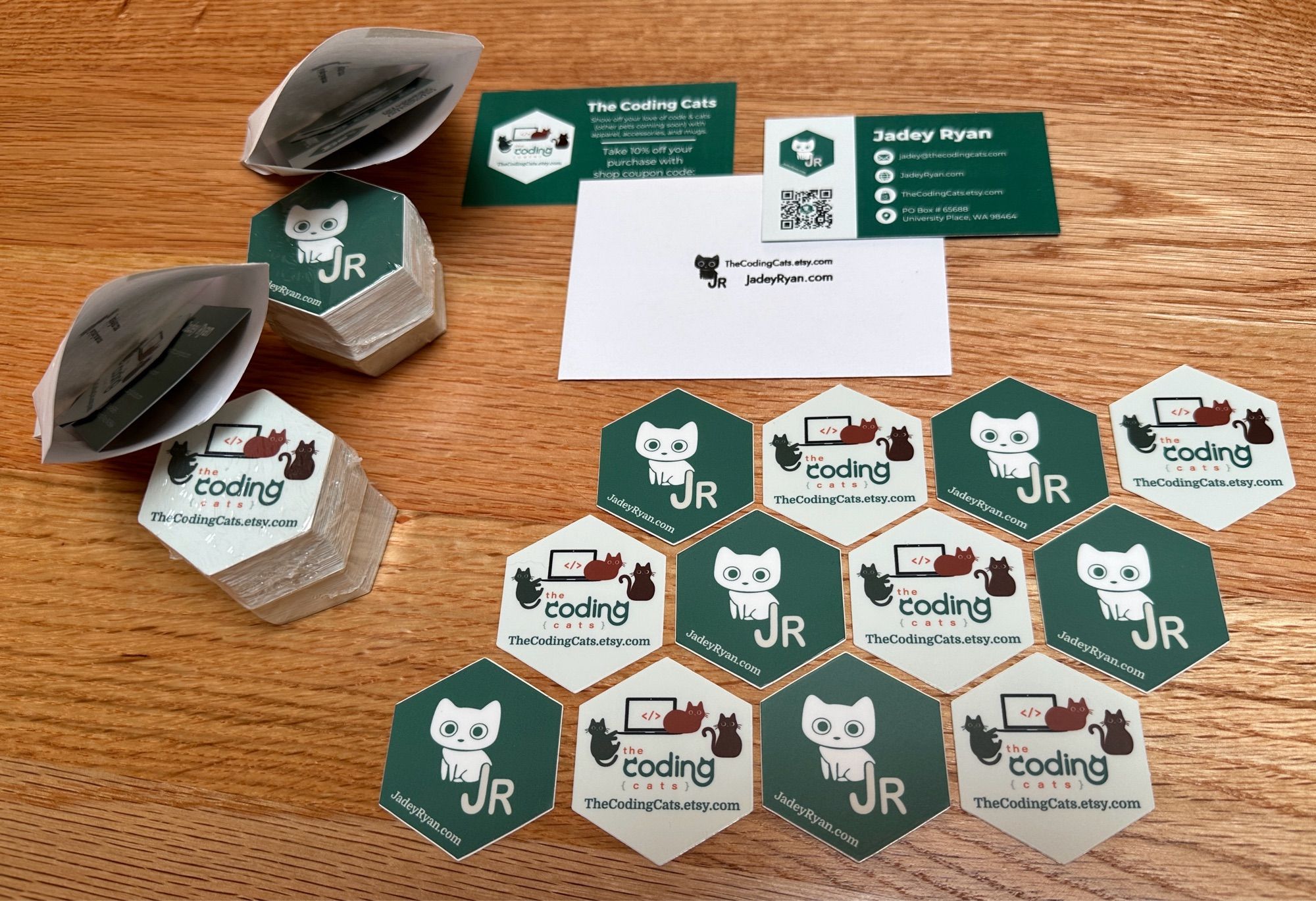 Jadey Ryan’s and The Coding Cat’s logos on hex stickers laid out with business cards and mini envelopes to collect more stickers!