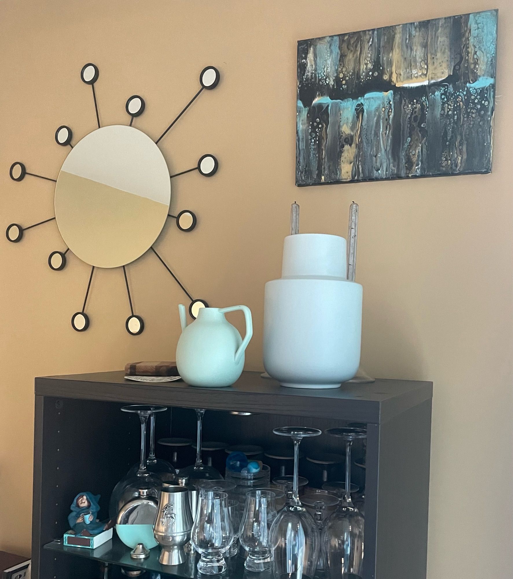 A turquoise blue, golden camel and black drip painting along with a Sputnik-kinda ikea mirror and the top of my bar with some pottery.