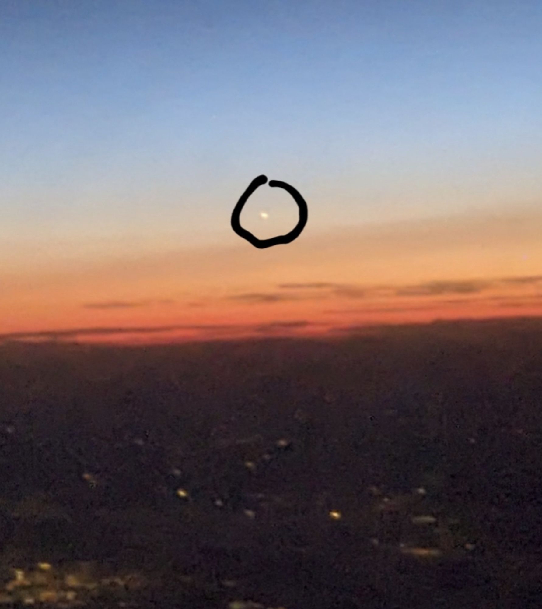 Sonnenuntergang vom Flugzeug aus mit einem hellen Lichtpunkt (eingekreist)