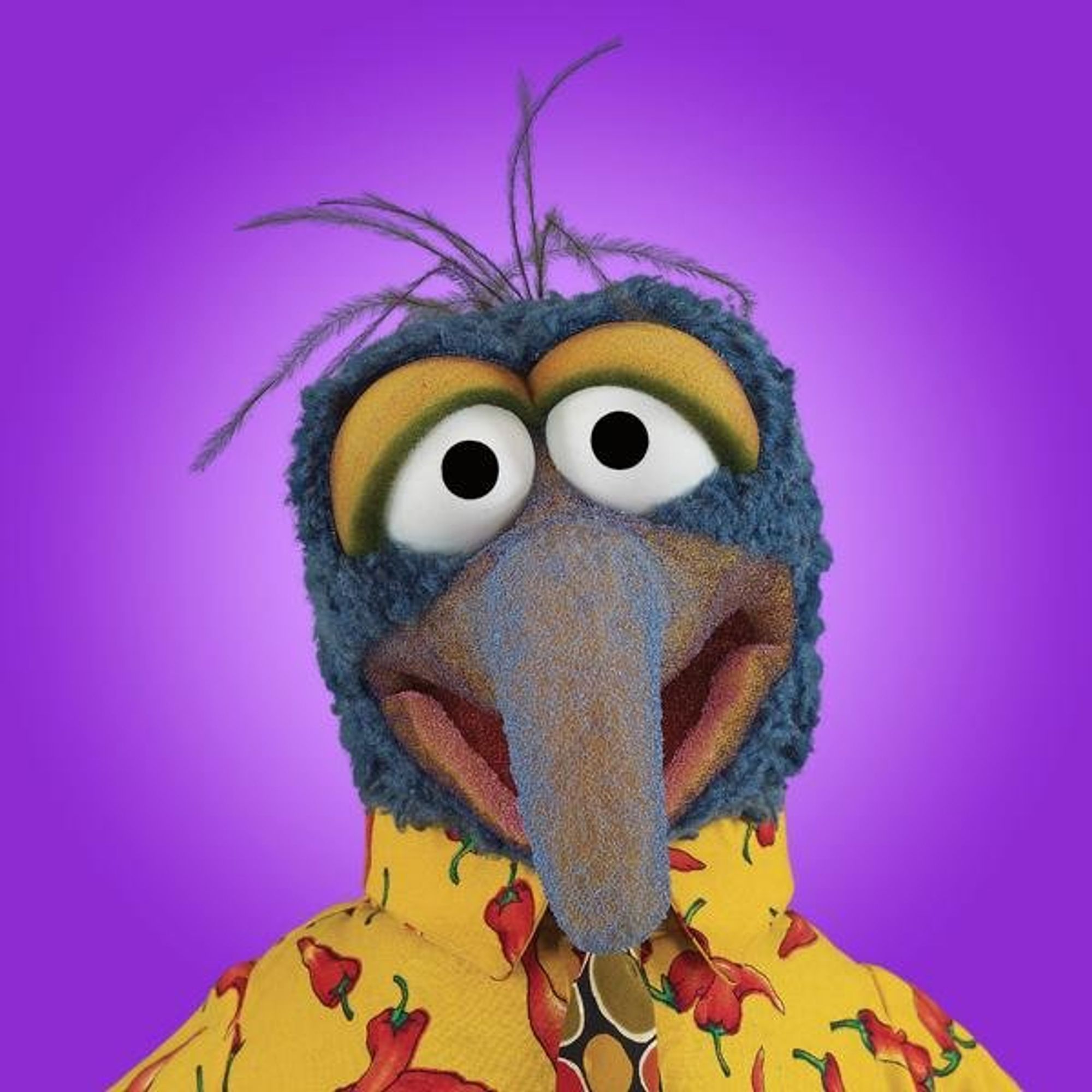 ID: Gonzo the Muppet looks directly at the camera while wearing a yellow red hot peppers button-up shirt against a purple backdrop.