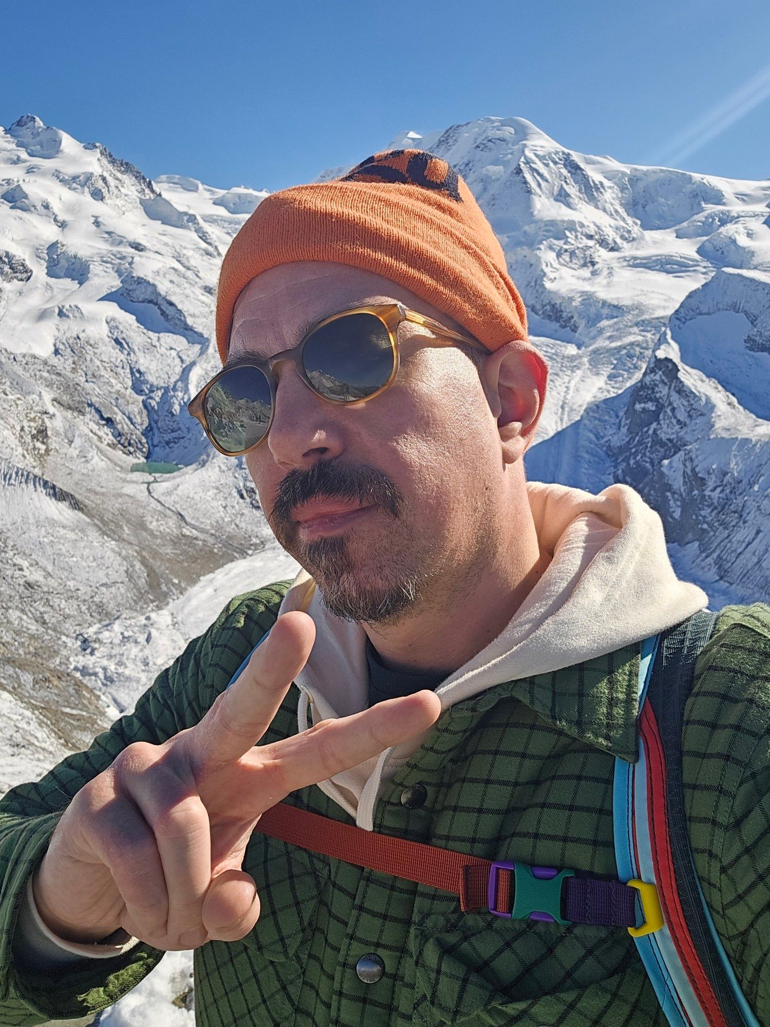 ME IN THE DAMN ALPS. Said Alps are behind me. I'm throwing up a peace sign in an orange beanie and sunglasses and wearing my Todd Snyder shirt jacket that I live in all winter. Rainbow striped backpack straps.