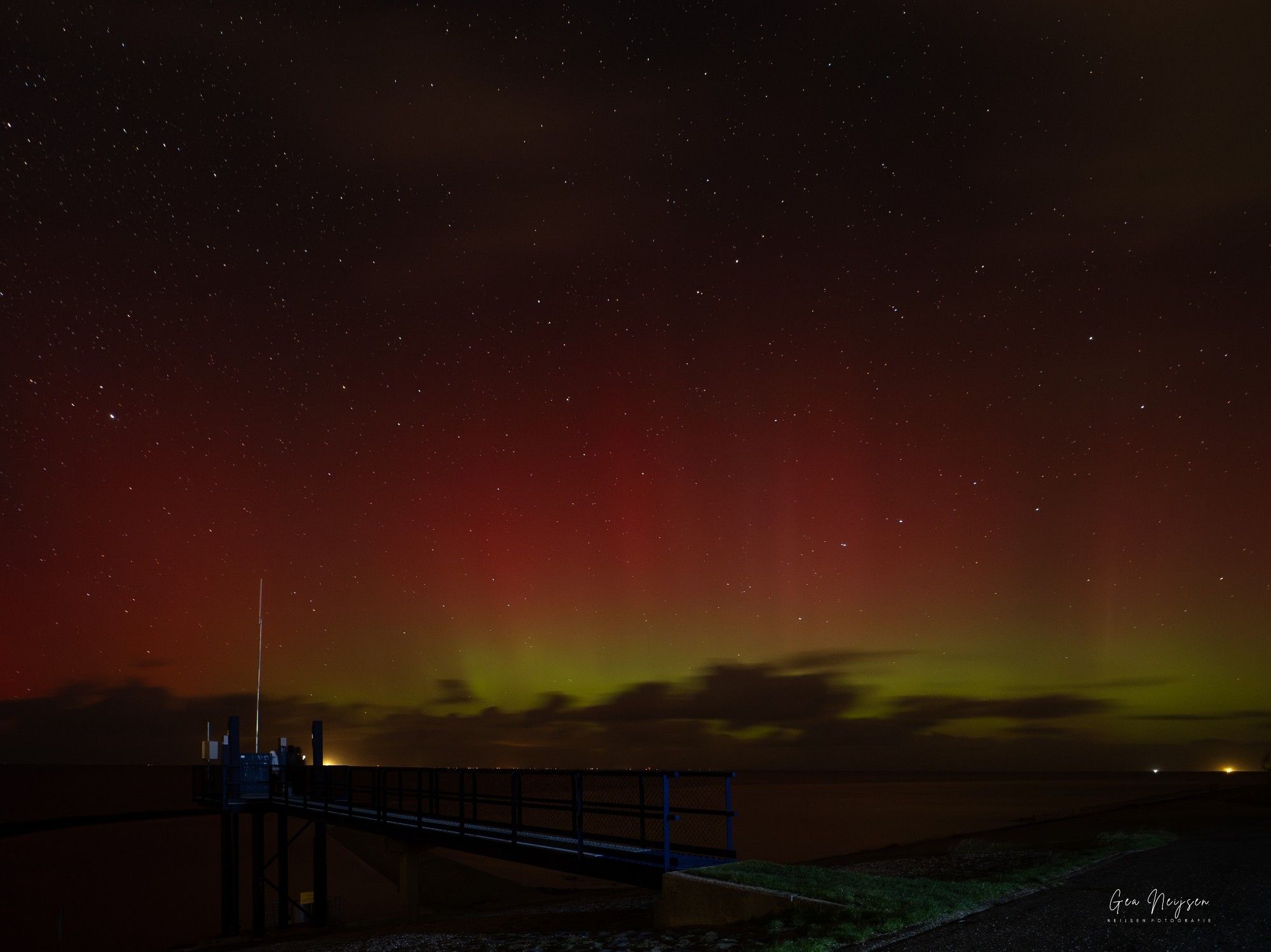 Rood groene lucht boven de Waddenzee. Op de voorgrond er soort loopbrug.