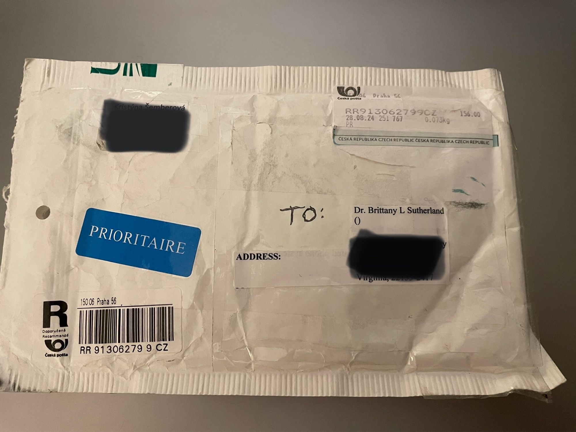 White envelope marked in English and Czech addressed to me but with both sender and receiver addresses blacked out. Envelope contains several dozen small clear plastic baggies of very tiny seeds.