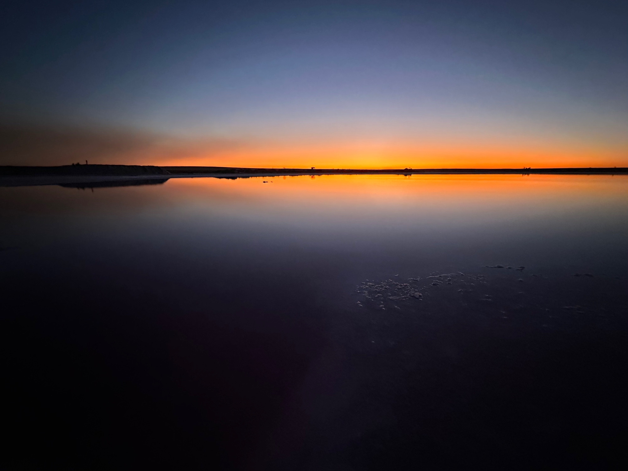 Looking out across a flat lake with sunset reflection