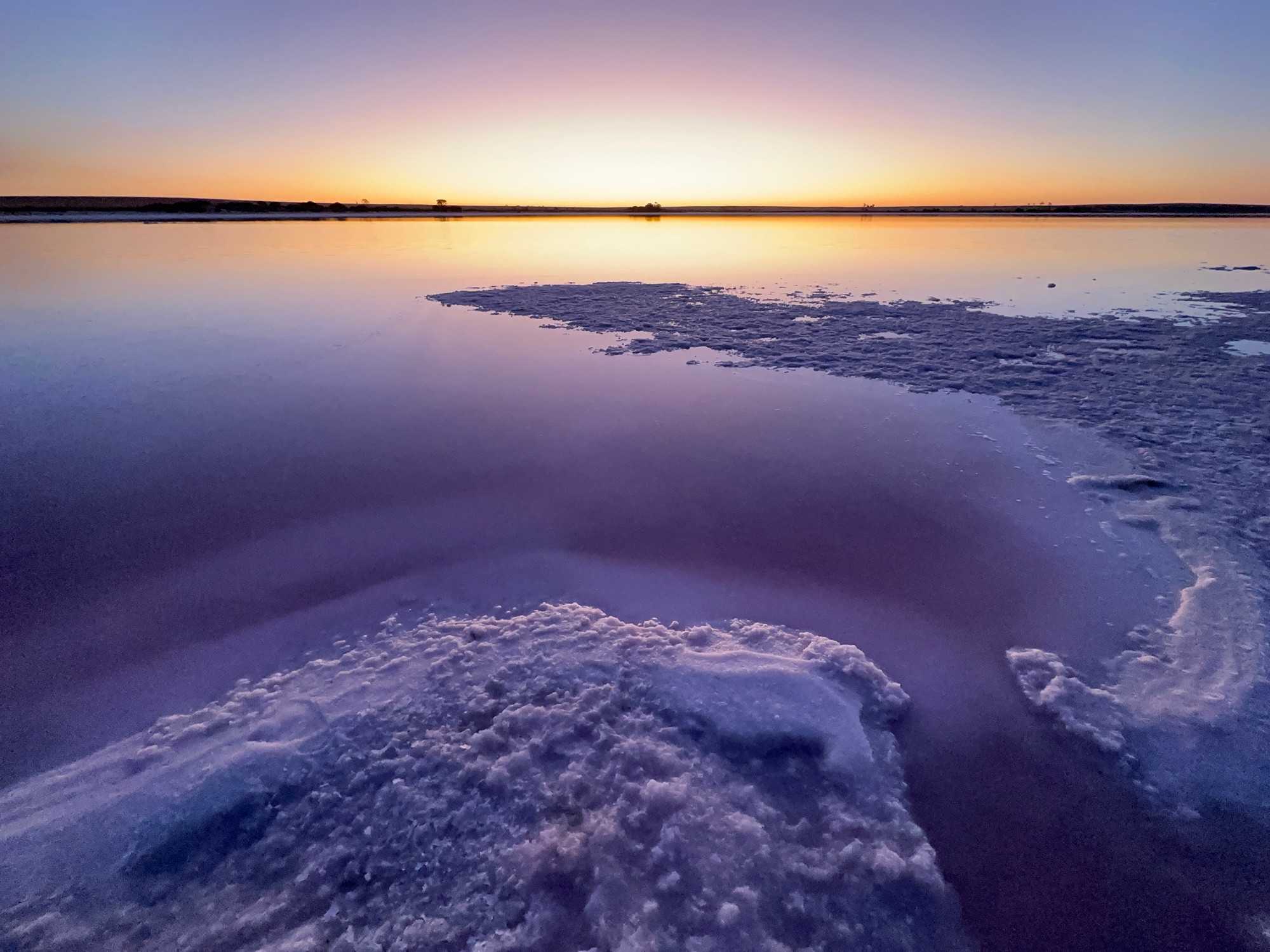 Looking out at a salt lake that has salt shorelines and is reflecting the colours of sunset