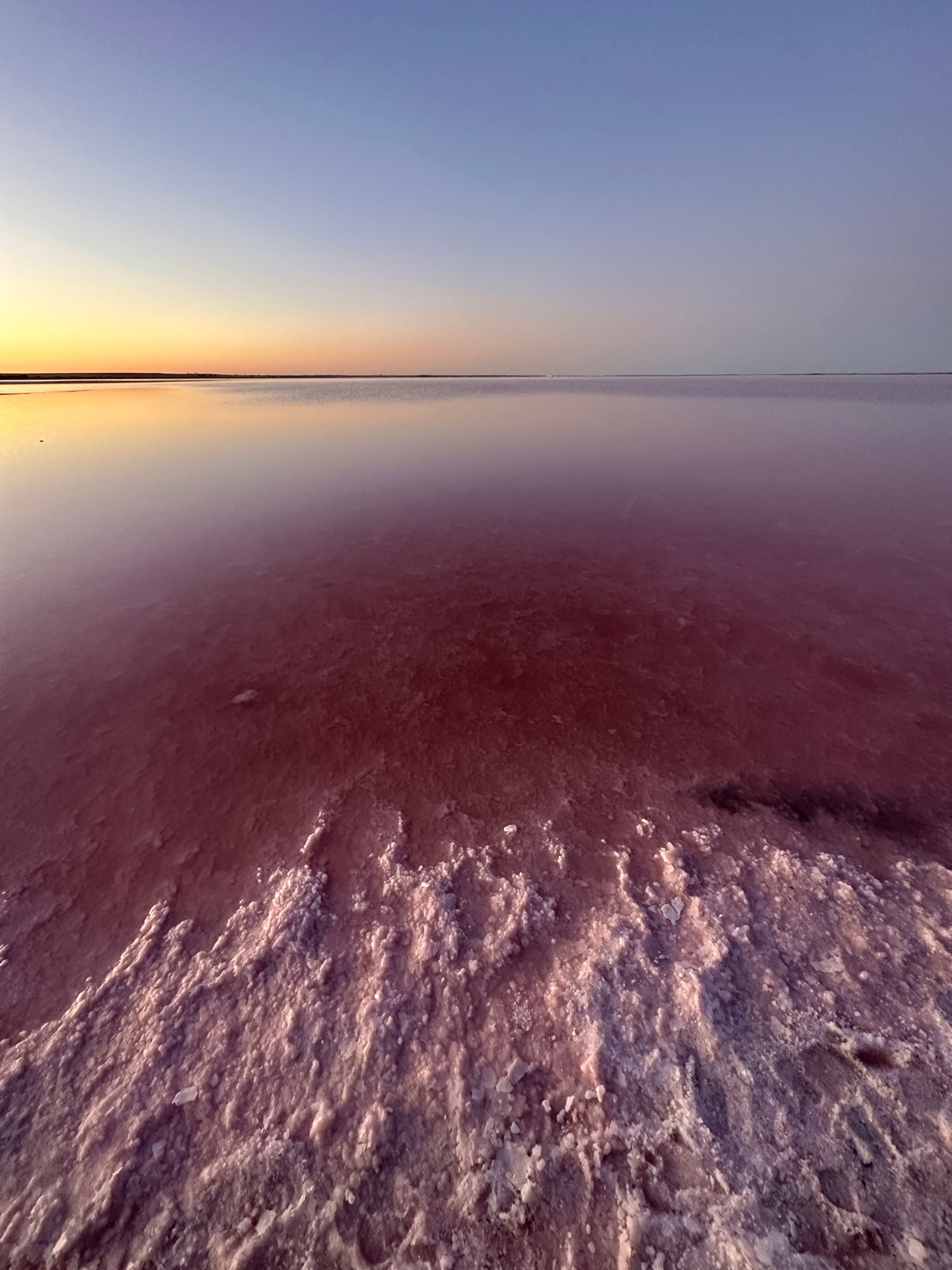 Looking out at a salt lake that has salt shorelines and is reflecting the colours of sunset