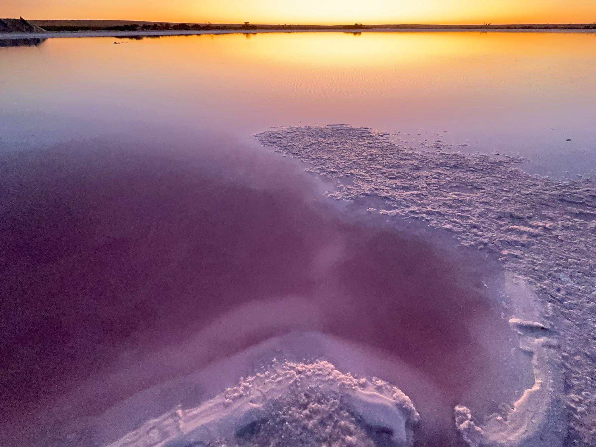 Looking out at a salt lake that has salt shorelines and is reflecting the colours of sunset