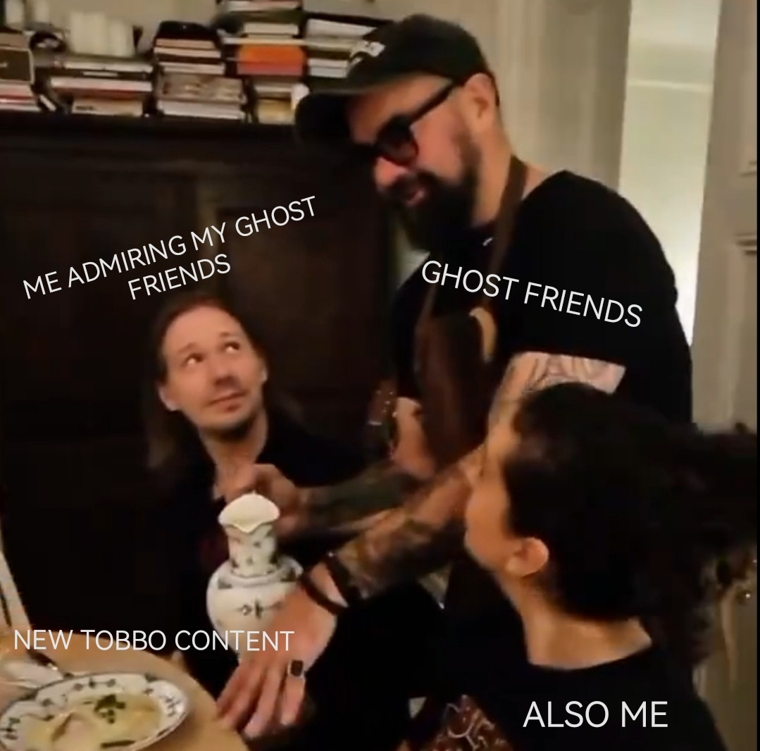 A screenshot of Tobias Forge and friends having a meal. Forge is looking up at a waiter lovingly. The text ME ADMIRING MY GHOST FRIENDS is above his head. The waiter appears to be talking about the meal they are all about to eat. The text GHOST FRIENDS is beside their head. A friend sitting next to Forge has their head turned away from the camera, but also looking up at the waiter. The text ALSO ME is covering them. The plate of food on the table has the text NEW TOBBO CONTENT above it.