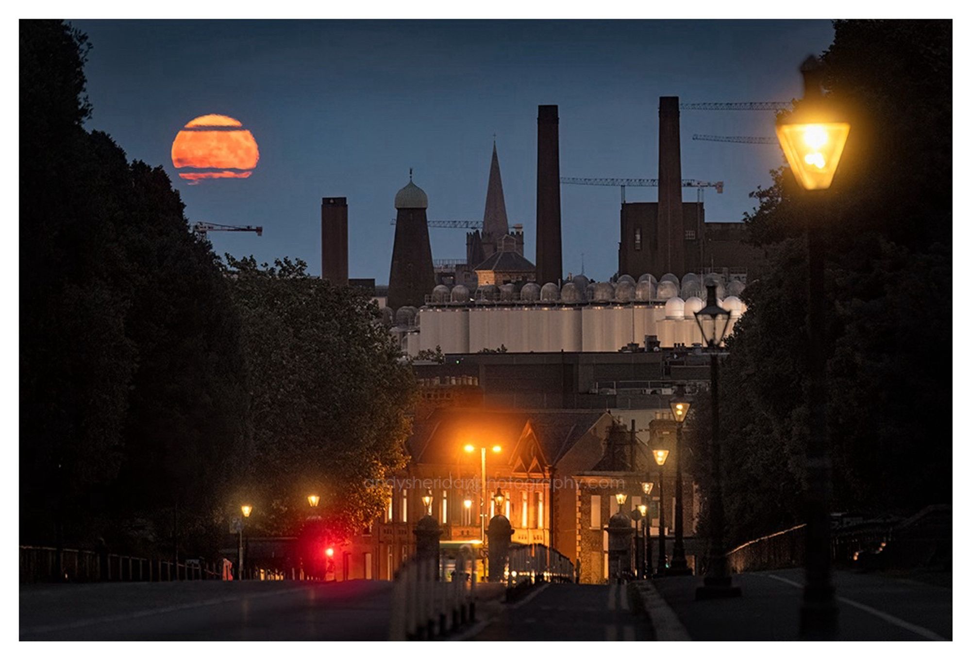 The three photos in this post show the rising full moon, called the Sturgeon Moon, rising over Dublin city. The photos were taken from Chesterfield Avenue, looking south-east.

In the foreground is the road, sloping down towards Parkgate Street and the gates to the Phoenix Park: to the left and right are the dark silhouettes of trees. The moon is rising behind some notable Dublin landmarks, including the Guinness brewery, the former Guinness Windmill on Thomas Street, and the spires of St. Catherine’s and St. Patrick’s.