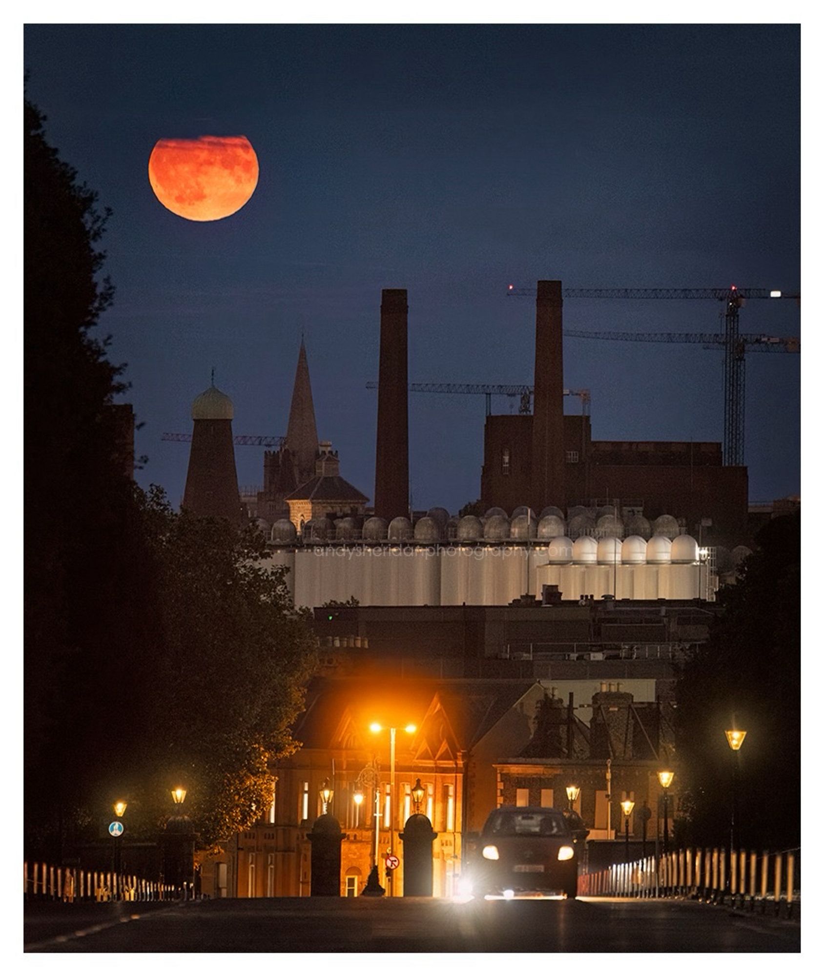 The three photos in this post show the rising full moon, called the Sturgeon Moon, rising over Dublin city. The photos were taken from Chesterfield Avenue, looking south-east.

In the foreground is the road, sloping down towards Parkgate Street and the gates to the Phoenix Park: to the left and right are the dark silhouettes of trees. The moon is rising behind some notable Dublin landmarks, including the Guinness brewery, the former Guinness Windmill on Thomas Street, and the spires of St. Catherine’s and St. Patrick’s.