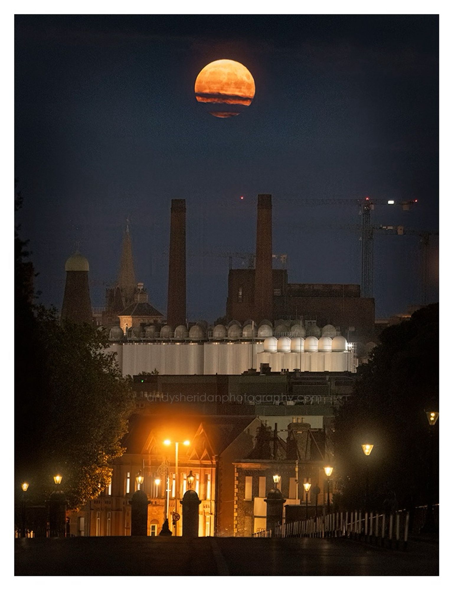 The three photos in this post show the rising full moon, called the Sturgeon Moon, rising over Dublin city. The photos were taken from Chesterfield Avenue, looking south-east.

In the foreground is the road, sloping down towards Parkgate Street and the gates to the Phoenix Park: to the left and right are the dark silhouettes of trees. The moon is rising behind some notable Dublin landmarks, including the Guinness brewery, the former Guinness Windmill on Thomas Street, and the spires of St. Catherine’s and St. Patrick’s.