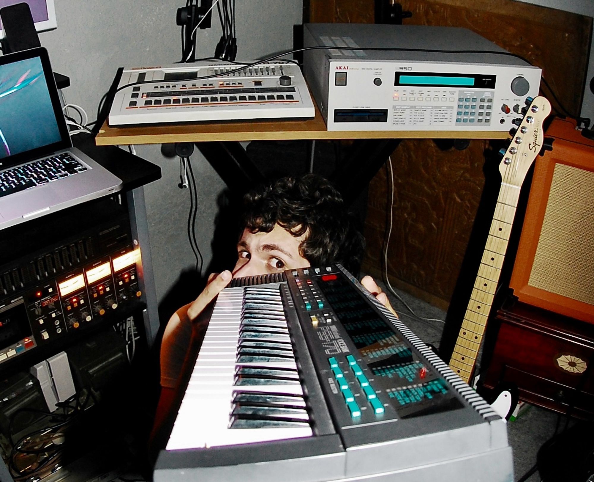 photo of a dumbass version of myself in front of a 707 and s-950 sampler. Absolute imbecile.  Curly hair, holding a cheap Yamaha toy piano in front of his face like a dumbass. Stupid mf sold a 707 and a s-950 probably for something stupid like rent. Smh.