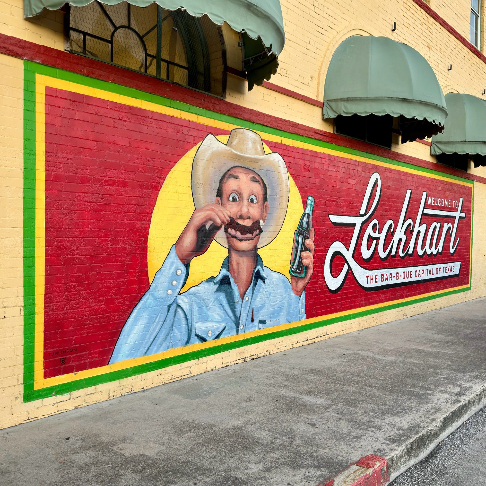 Mural that reads “lockhart the barbecue capital of Texas” with  cowboy making a smiley face with a rib